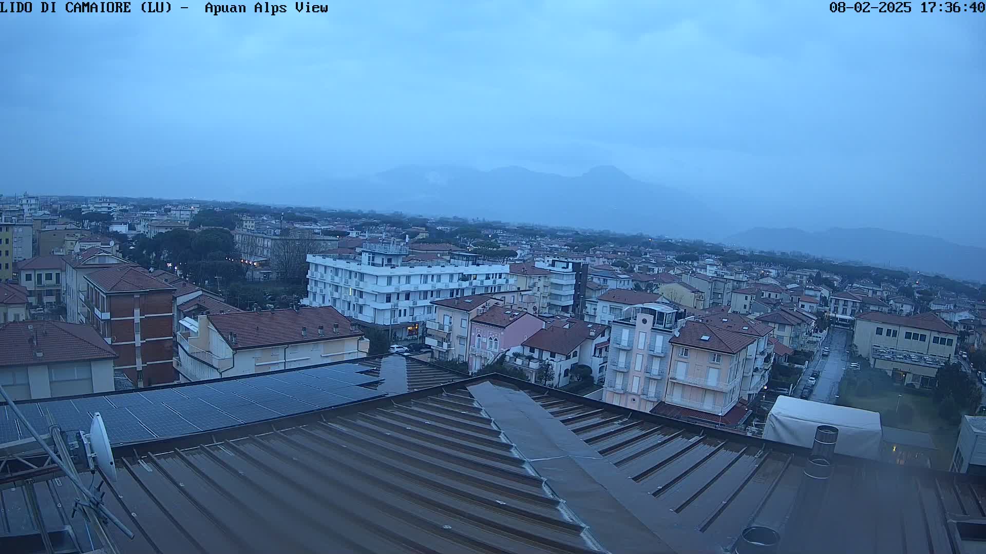 A wet rooftop overlooks a town under an overcast sky, with mountains visible in the distance.