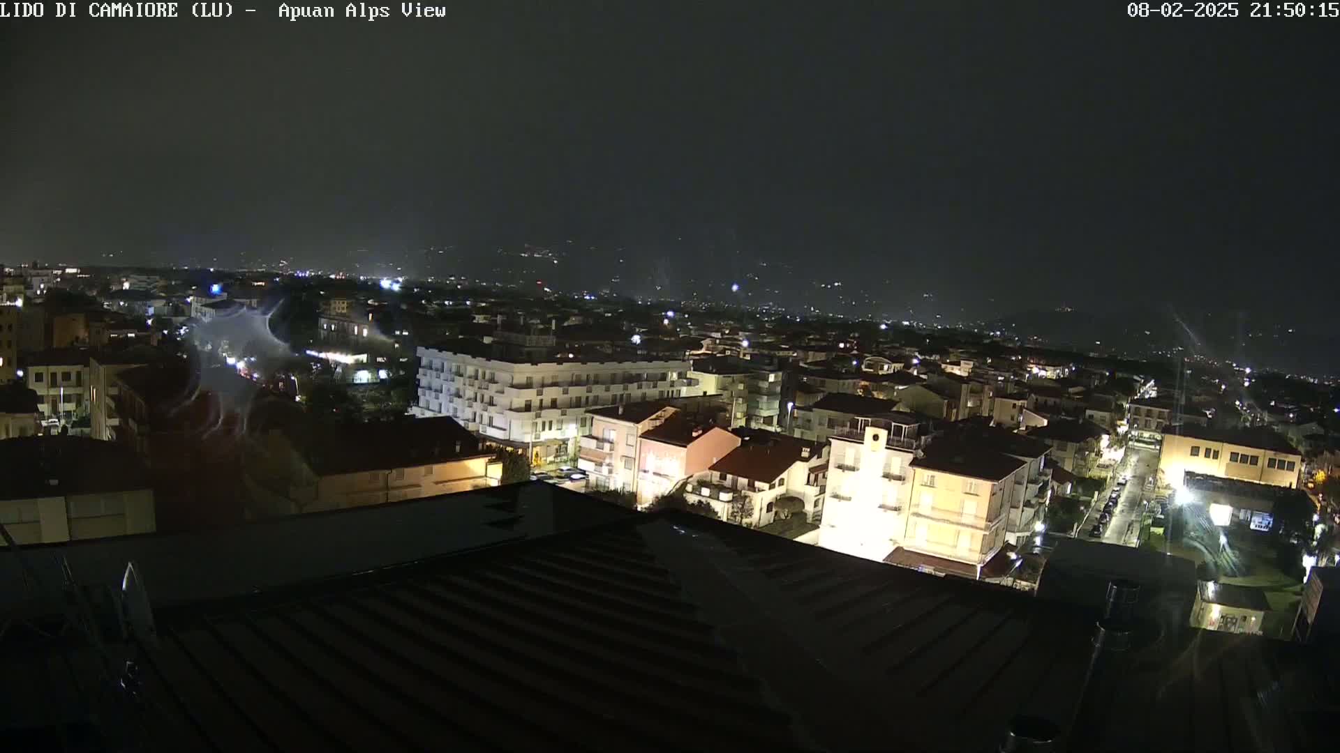 A nighttime view of a town illuminated by streetlights and building lights under a dark, possibly stormy sky.