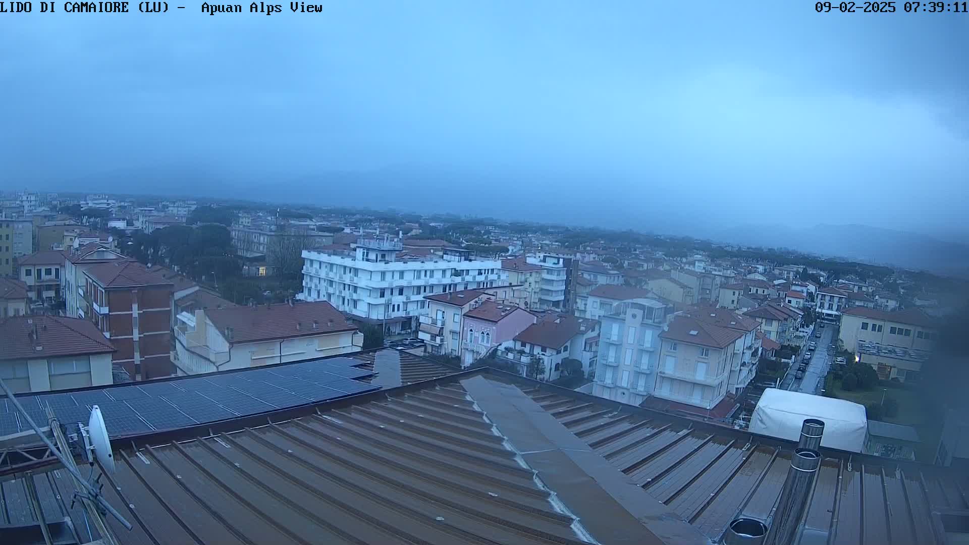 A wet rooftop overlooks a town under an overcast sky.
