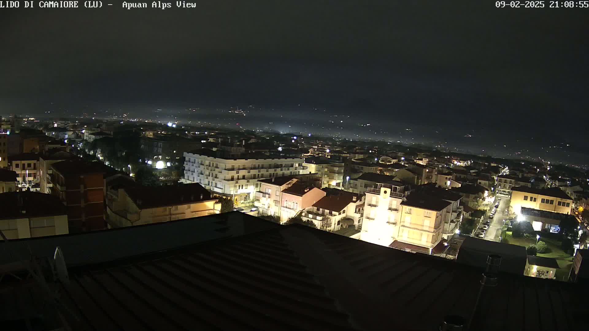 A nighttime aerial view of a town illuminated by streetlights, with a hazy, dark sky in the background.
