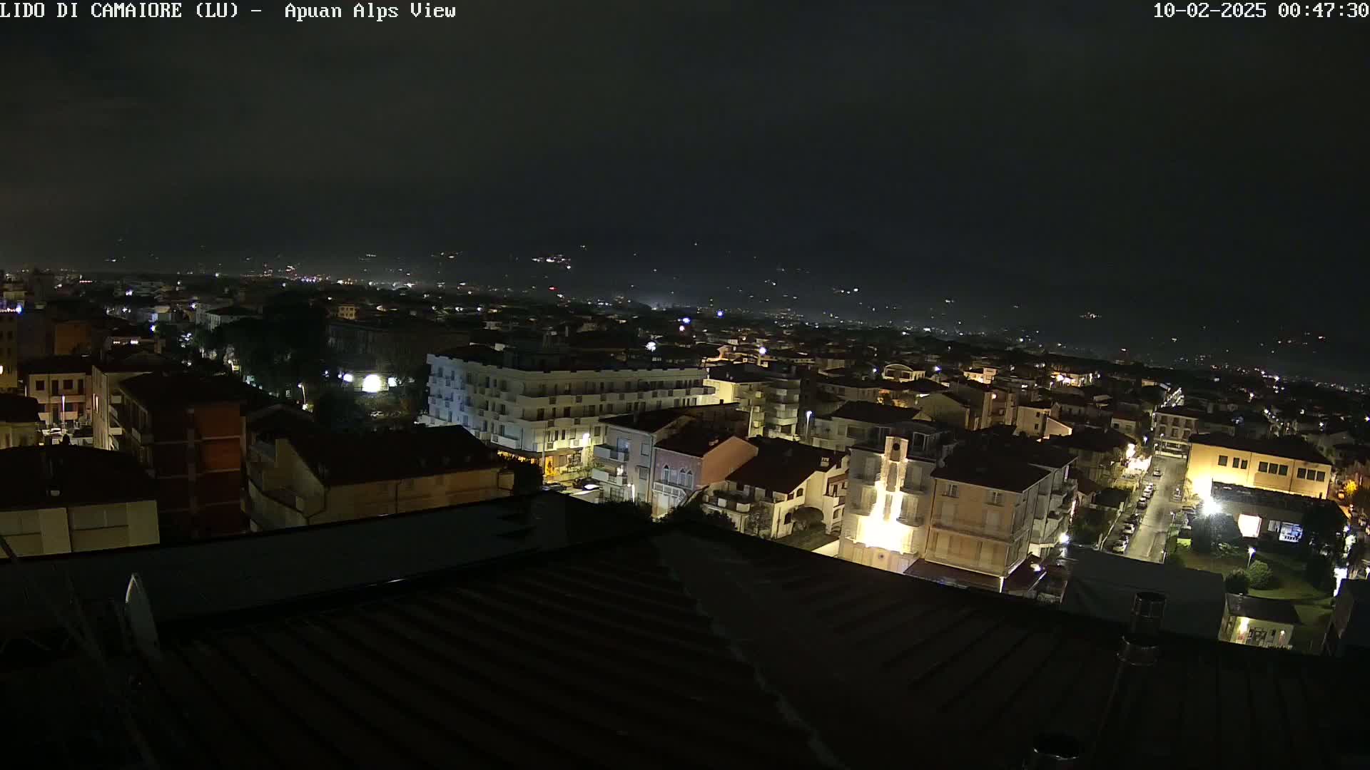 A nighttime aerial view of a town, illuminated by streetlights, with a dark, clear sky in the background.