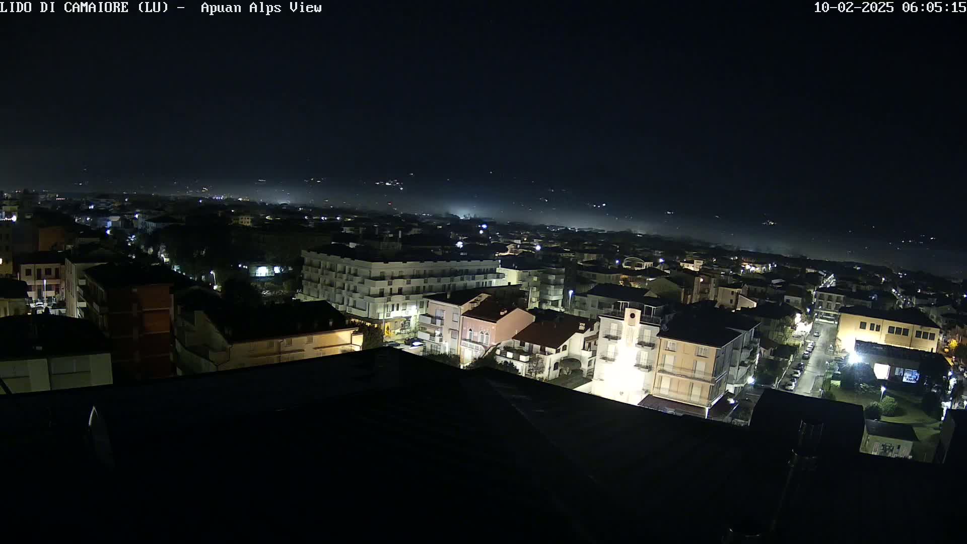 A nighttime, high-angle view of a town illuminated by streetlights, with a hazy or foggy horizon in the distance.