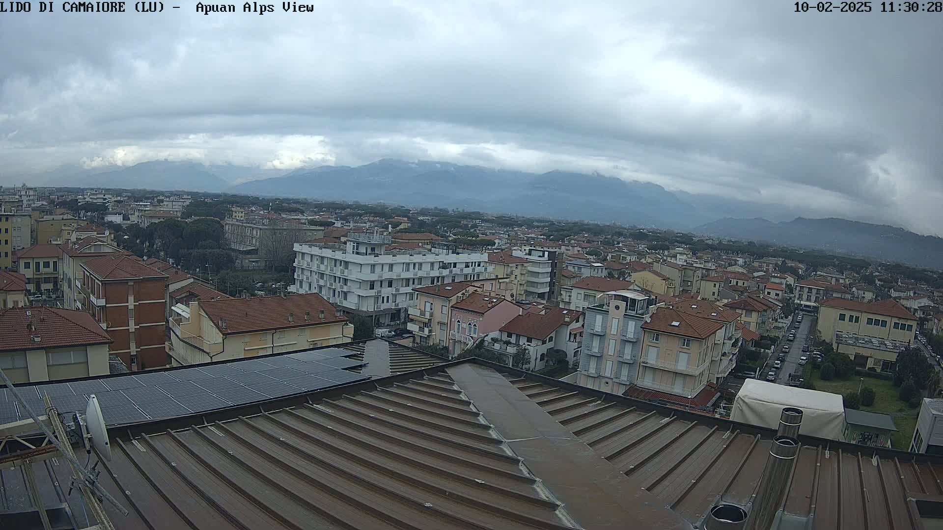 A rooftop view of a town shows overcast skies and distant mountains, with many buildings visible.