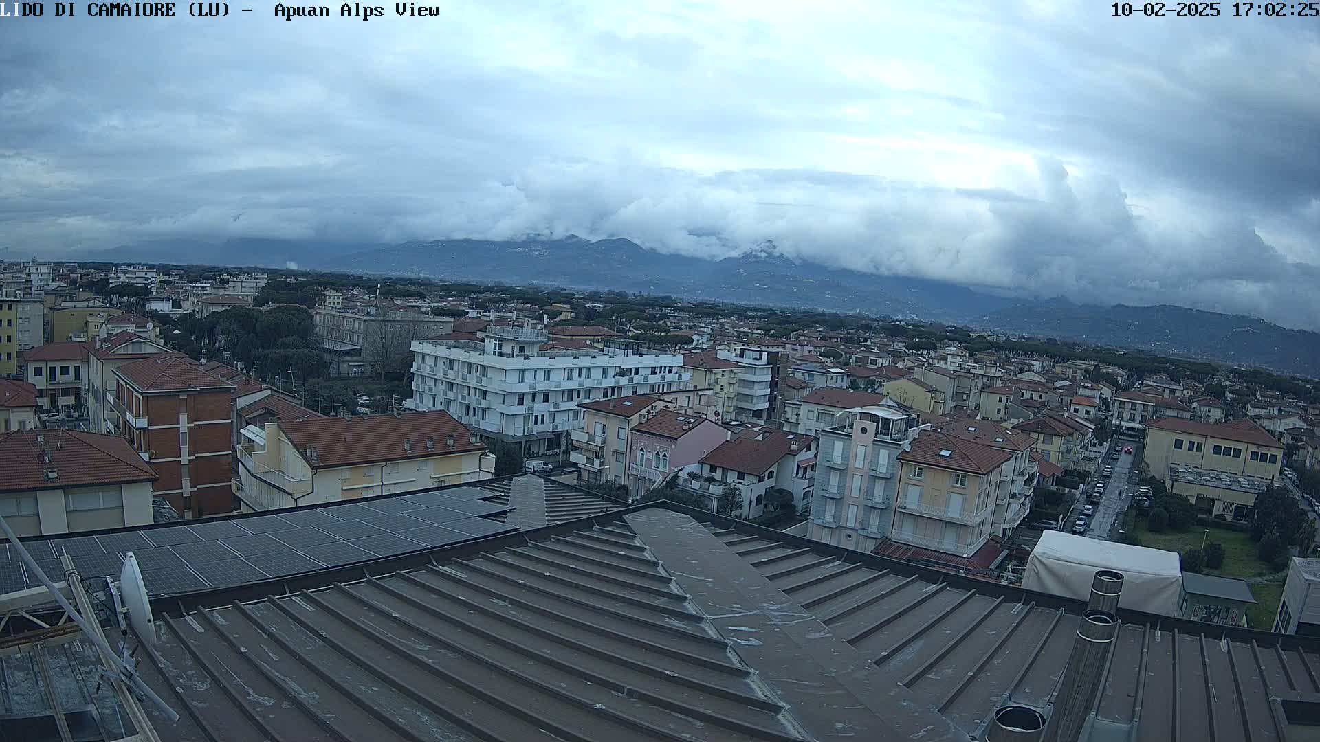 A cloudy day reveals a cityscape of low-rise buildings extending to distant mountains under a mostly overcast sky.