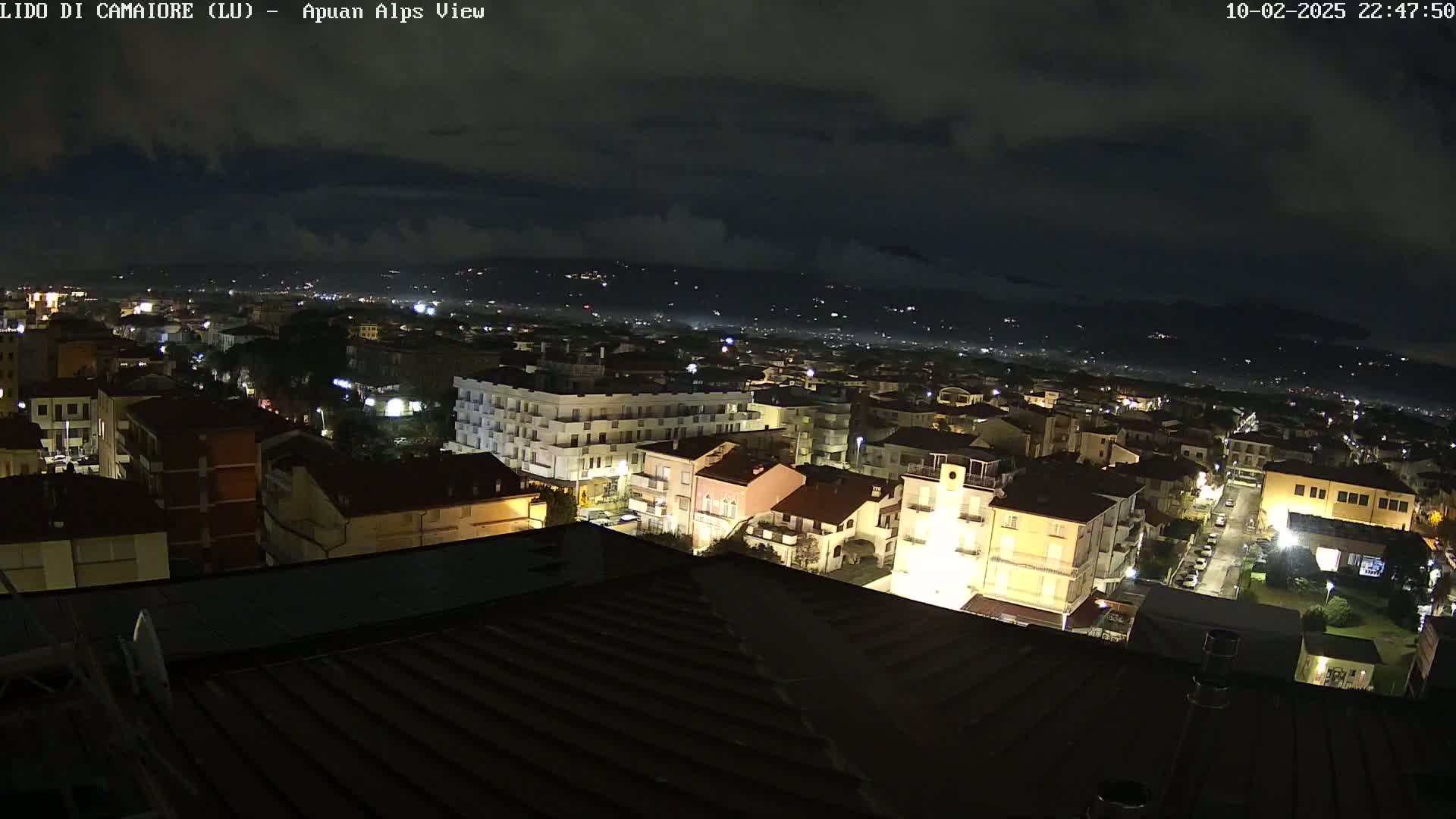 A nighttime view of a town with buildings illuminated, under a cloudy sky.