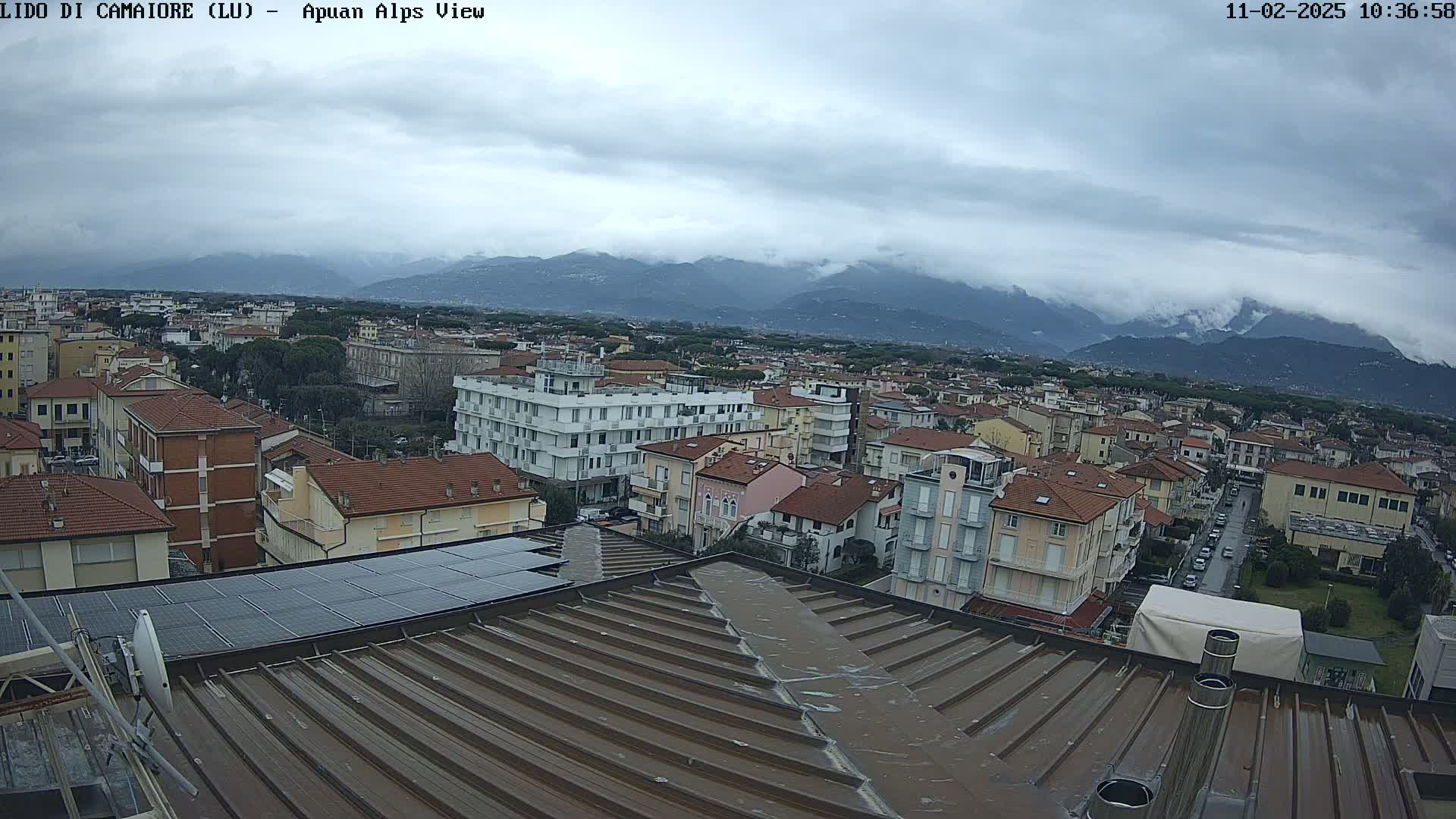 A view from a rooftop shows a town under a cloudy sky, with mountains in the distance.