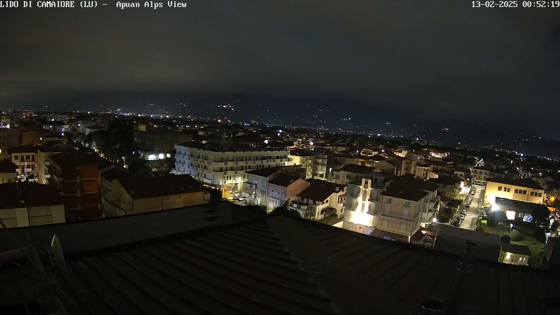 A nighttime, aerial view of a town shows numerous buildings illuminated against a dark, overcast sky.