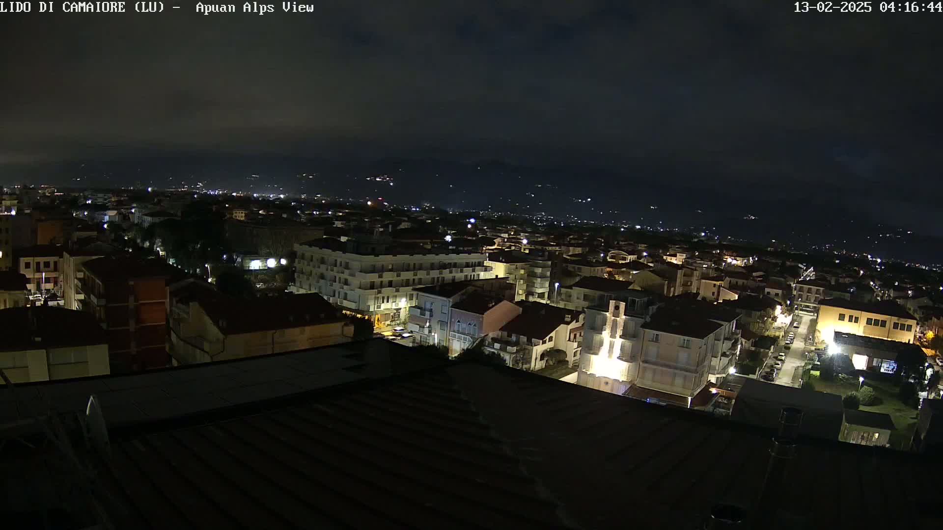 A nighttime view of a town nestled against mountains under a dark, cloudy sky.