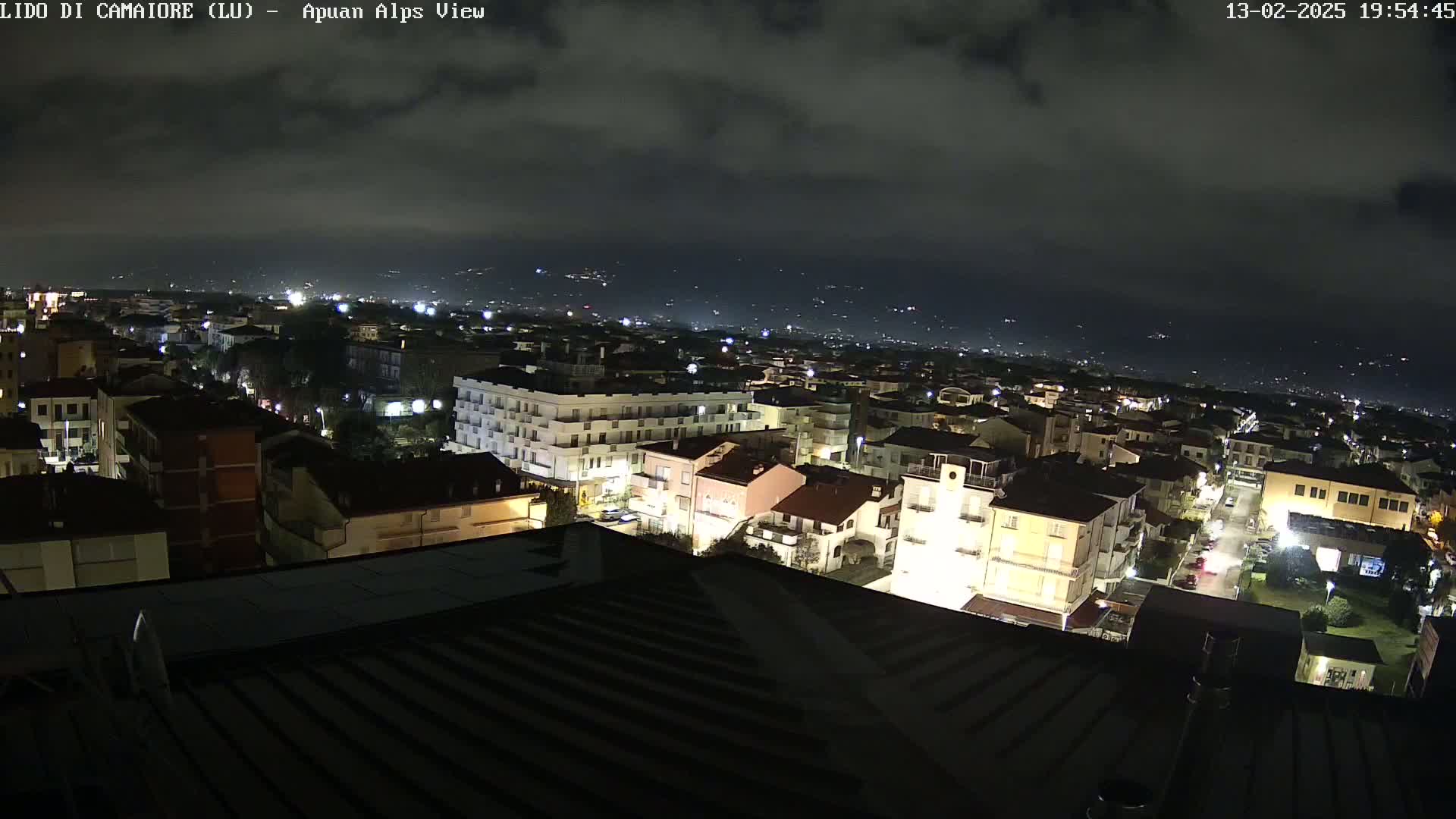 A nighttime view of a town illuminated by streetlights, under a cloudy sky.