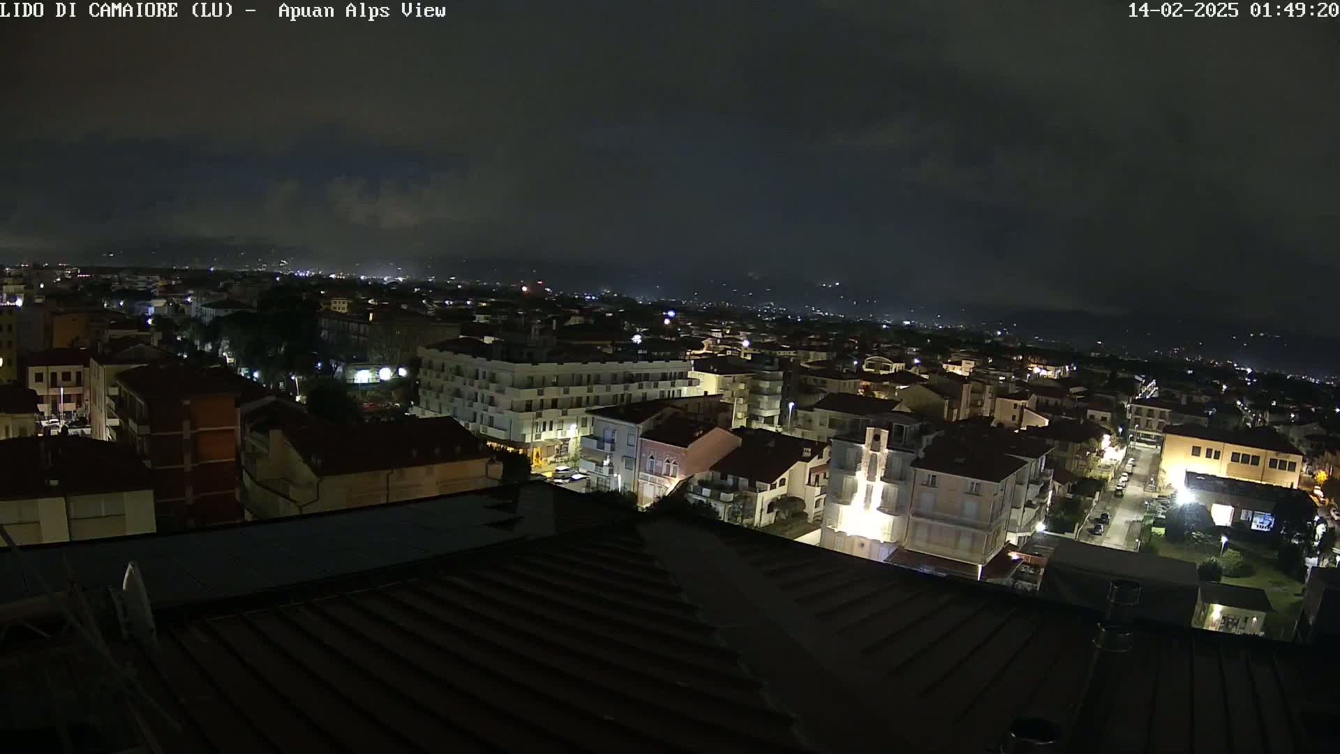 A nighttime aerial view of a town with dimly lit buildings under a cloudy sky.
