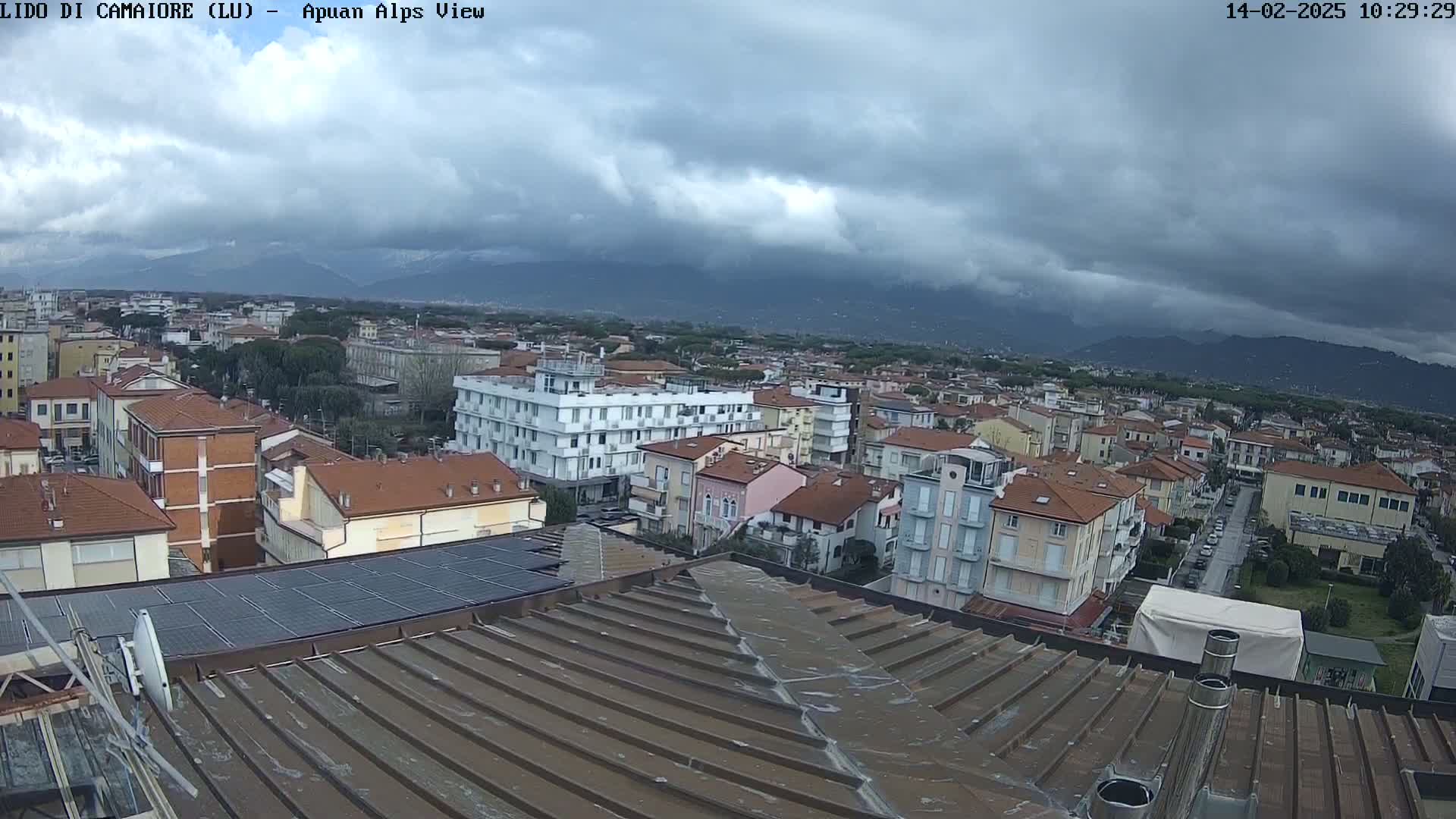 A rooftop view of a town under a cloudy sky, with mountains in the distance.