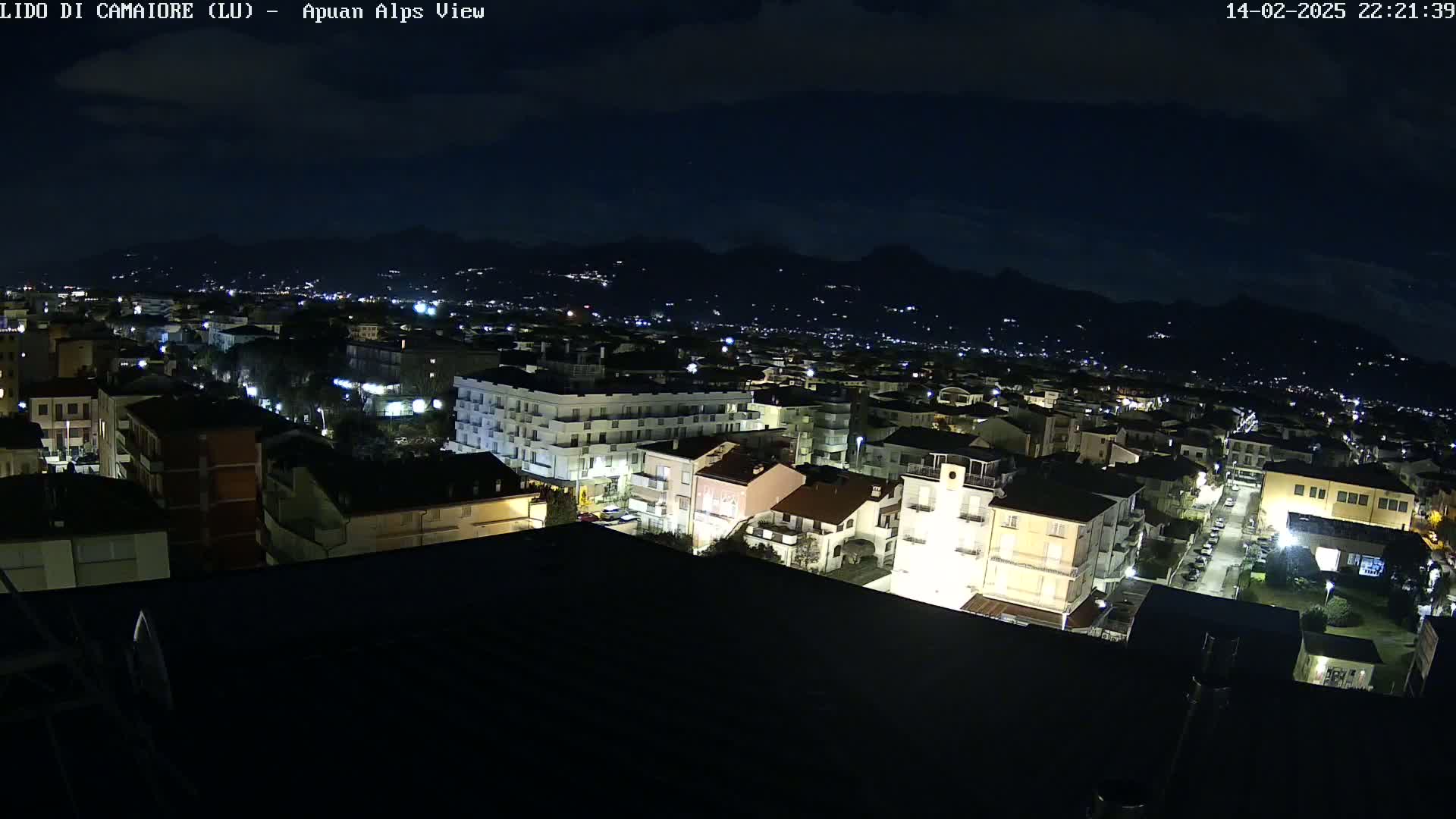 A nighttime, high-angle view of a town illuminated by streetlights, with mountains visible in the distance under a dark sky.