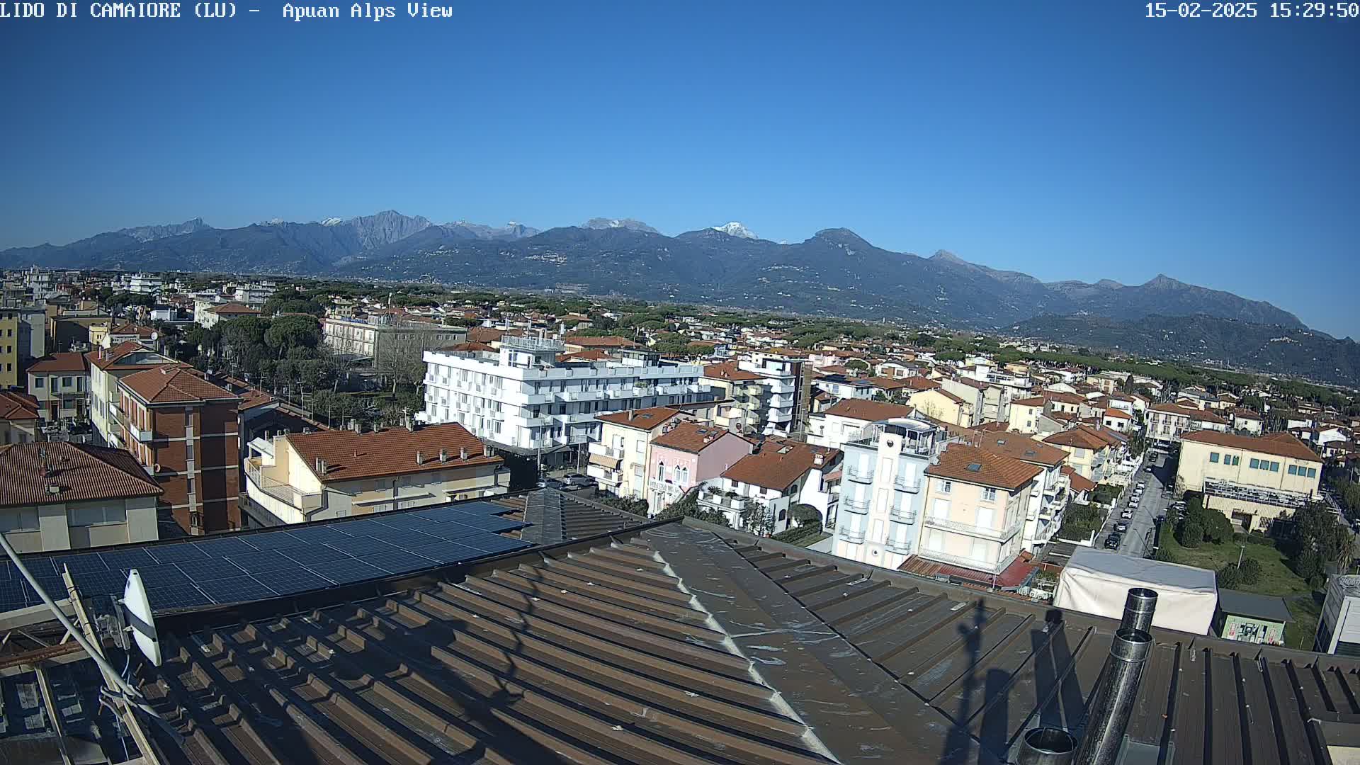 A rooftop view of a town nestled at the foot of snow-capped mountains under a clear blue sky.