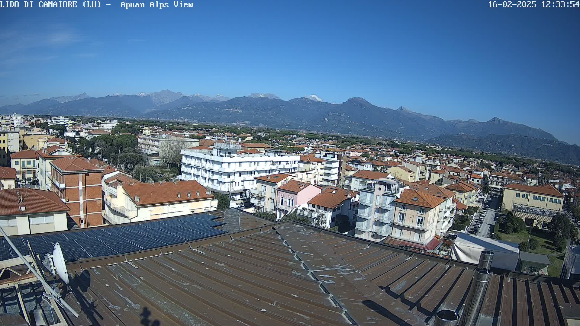 A rooftop view of a town nestled against a backdrop of snow-capped mountains under a clear blue sky.