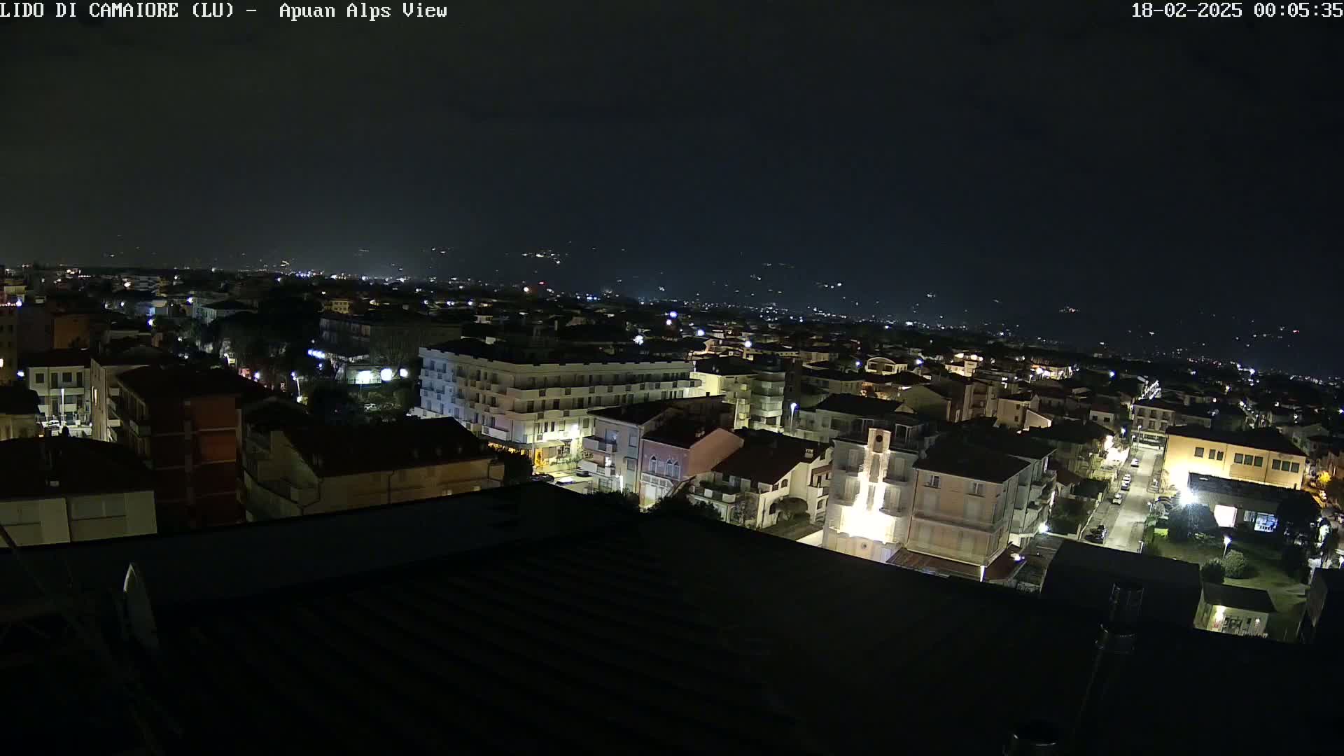 A nighttime, aerial view shows a town with illuminated buildings and streets, under a clear, dark sky.