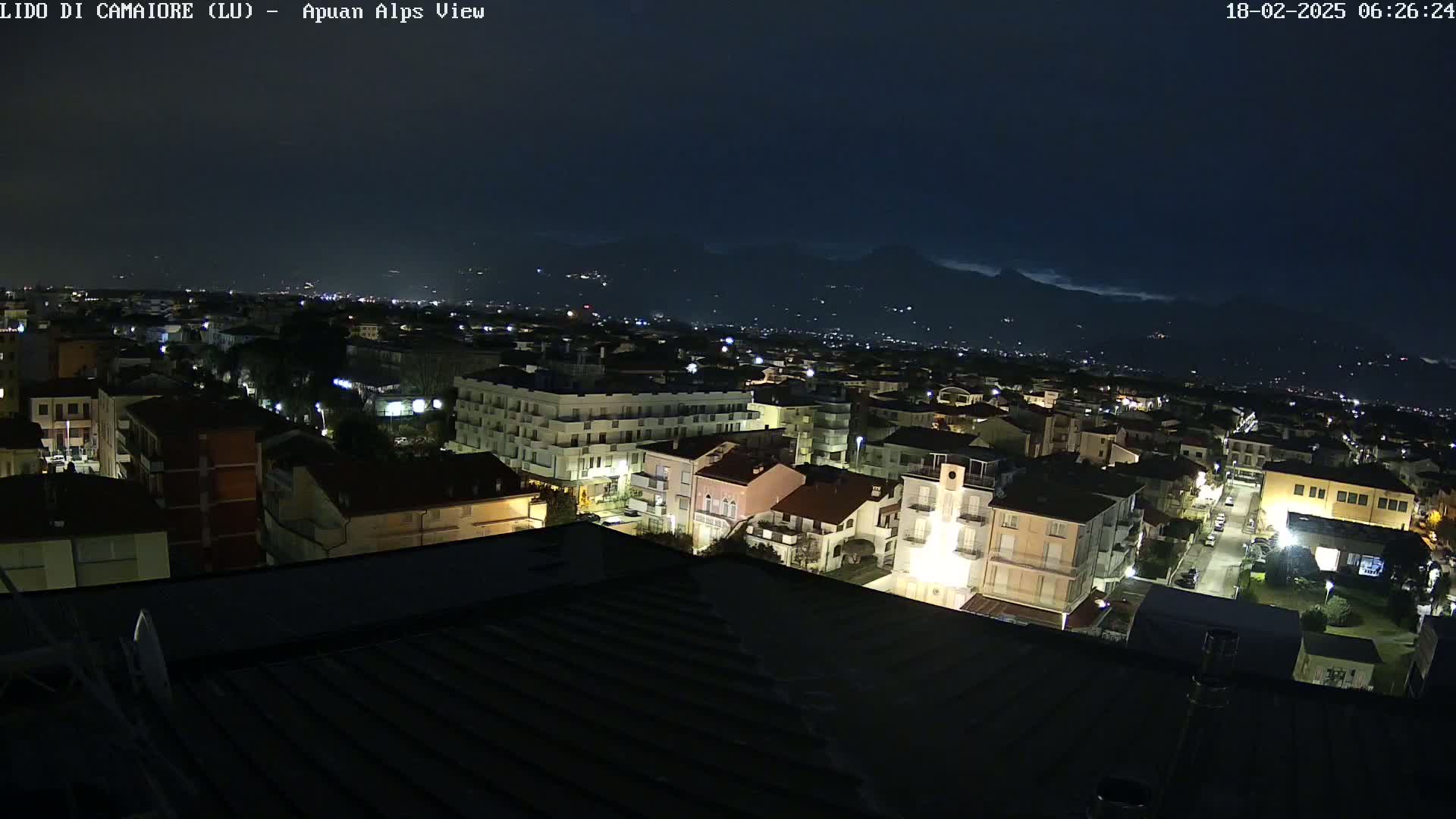 A nighttime view of a town illuminated by streetlights, with a mountain range visible in the distance under a dark sky.