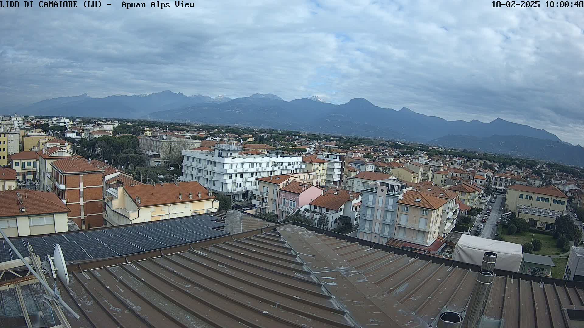 A rooftop view of a town under a cloudy sky, with a mountain range visible in the distance.