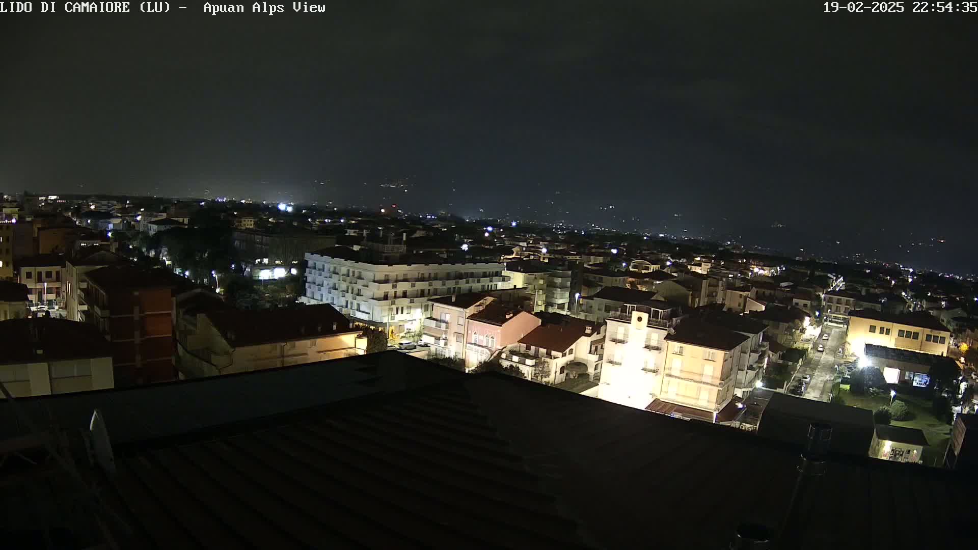 A nighttime, high-angle view of a town with buildings illuminated by streetlights, extending to a dark, distant horizon under a clear, dark sky.