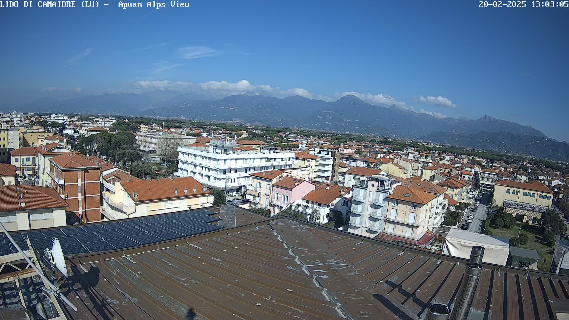 A rooftop view of a town on a sunny day, overlooking a range of mountains in the distance.