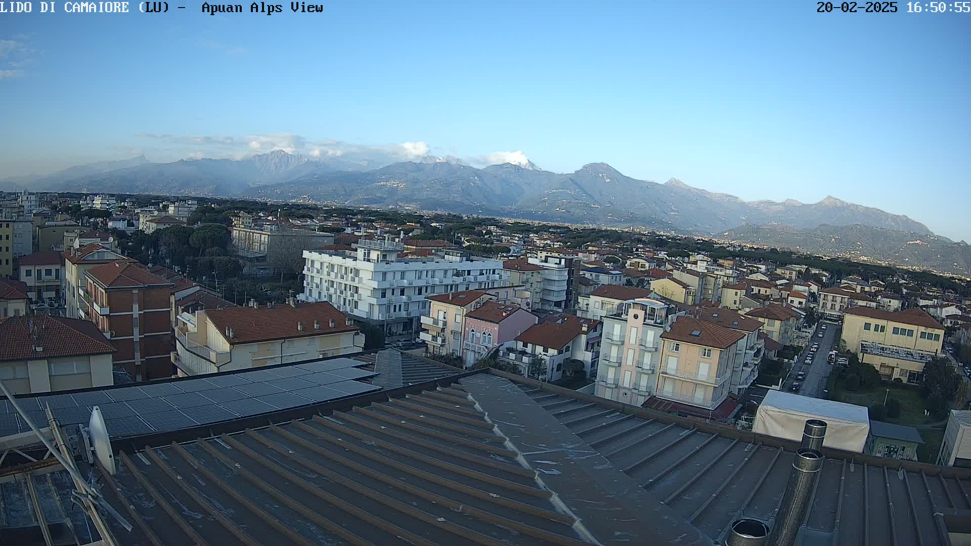 A rooftop view of a town, under a clear blue sky, shows a mountain range in the background.