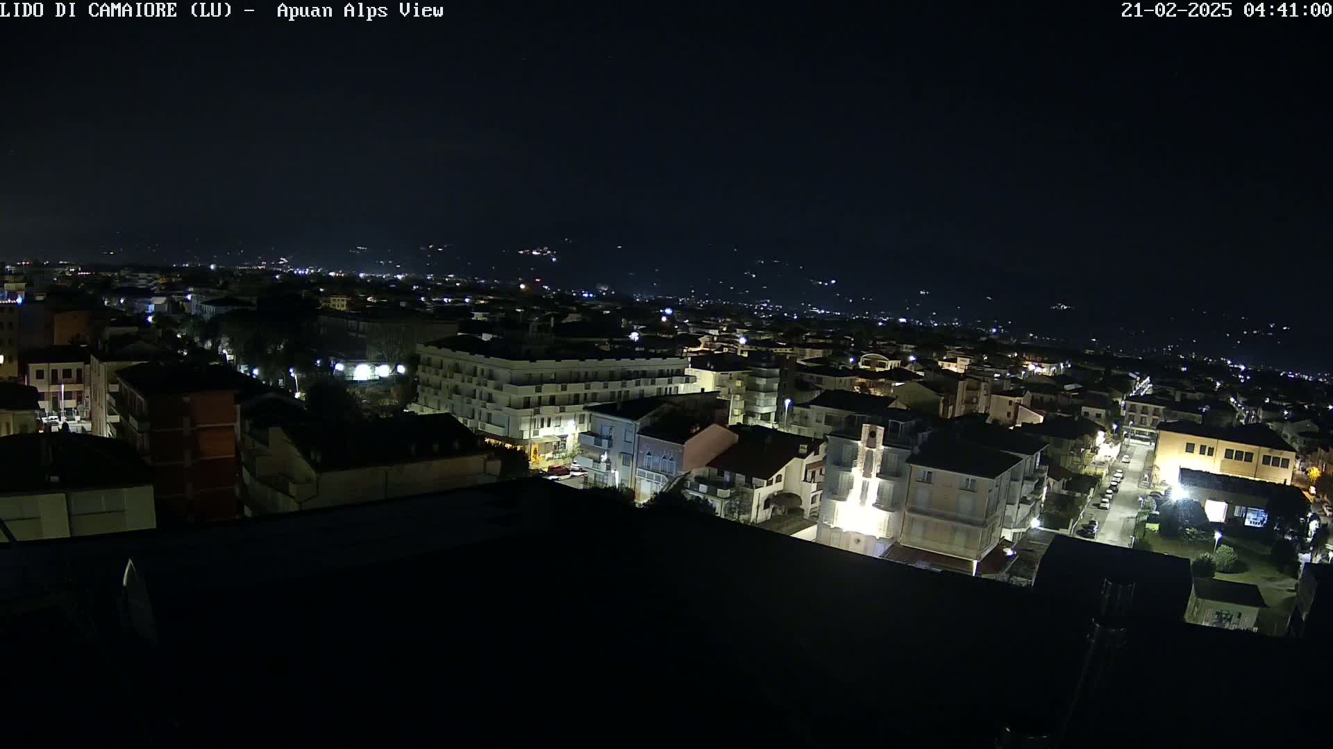 A nighttime aerial view shows a town with illuminated buildings under a clear, dark sky.
