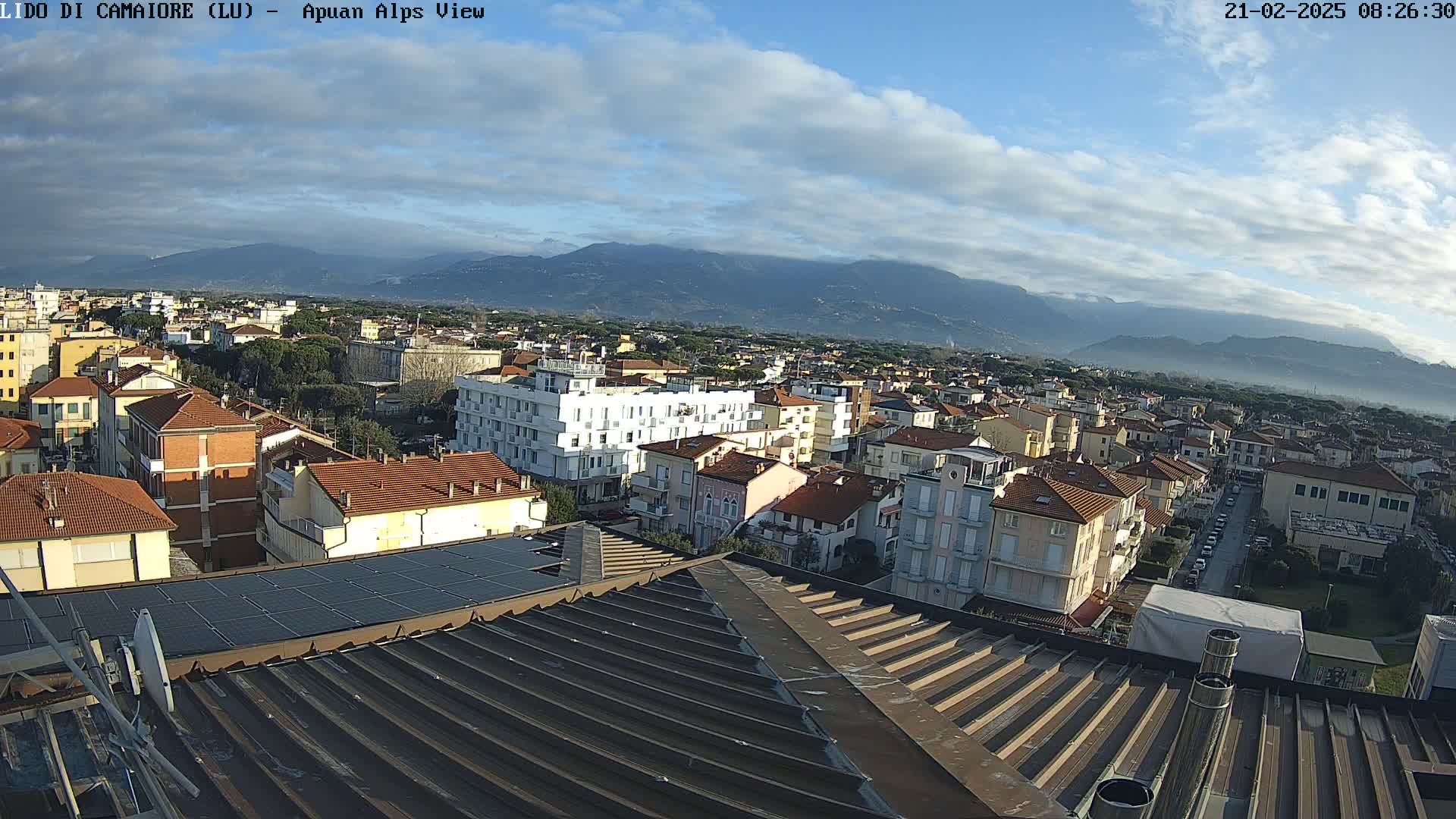 A partly cloudy day reveals a cityscape of low-rise buildings, extending to distant mountains.