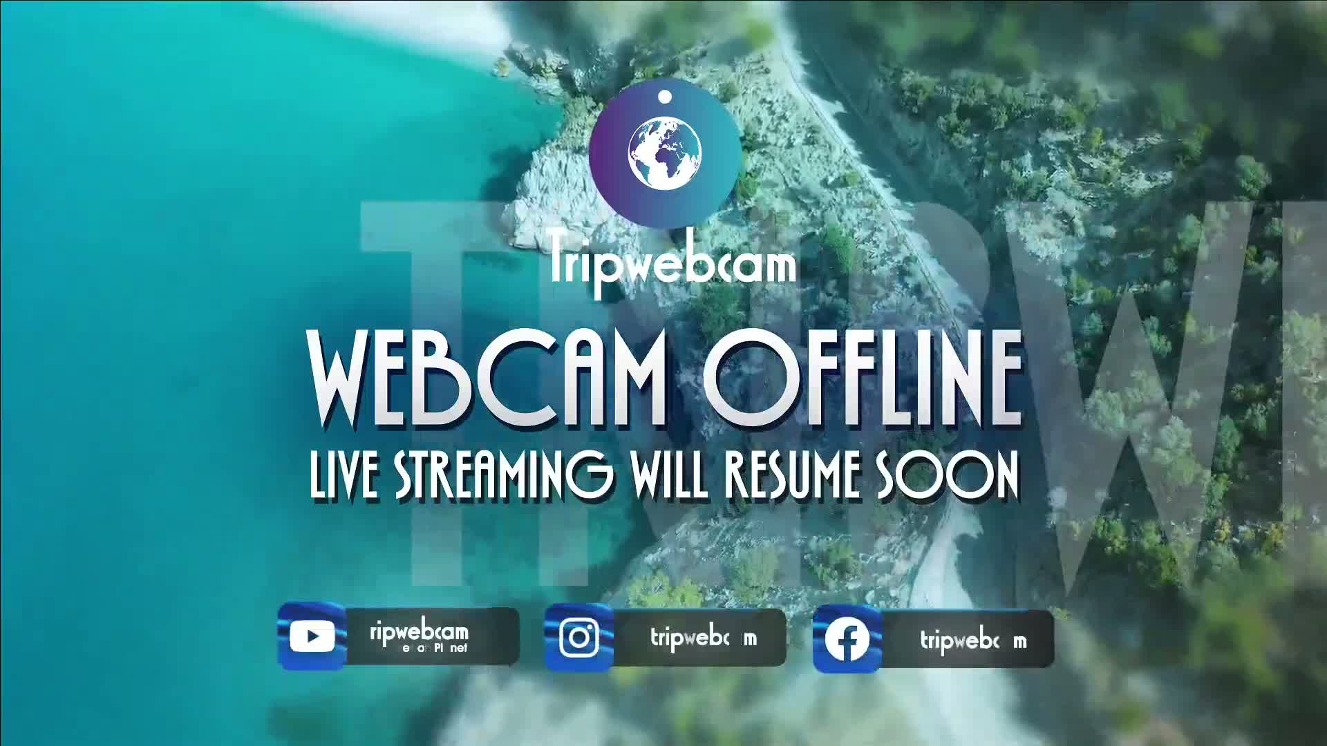 An aerial view of a rocky coastline meeting turquoise water, overlaid with a message indicating that a webcam is temporarily offline.