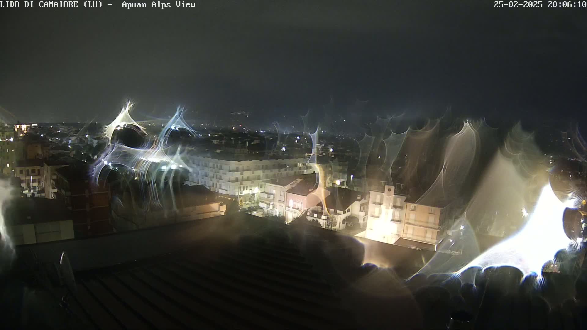 A nighttime view of a city illuminated by lights, seen through a rain-streaked window.