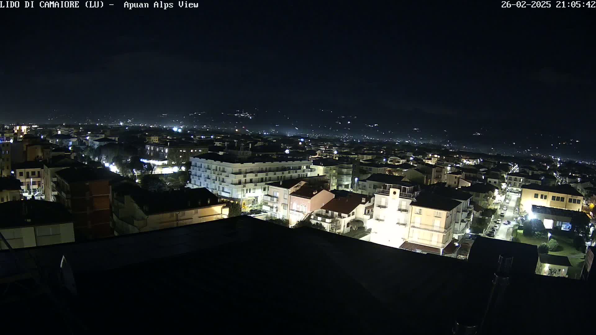 A nighttime aerial view of a town shows many buildings with lights on, under a clear, dark sky.