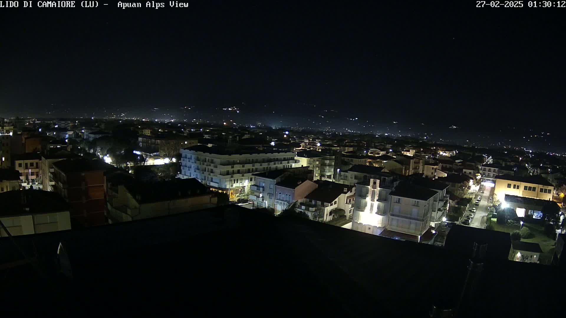 A nighttime aerial view of a city with dimly lit buildings and streets, under a clear, dark sky.