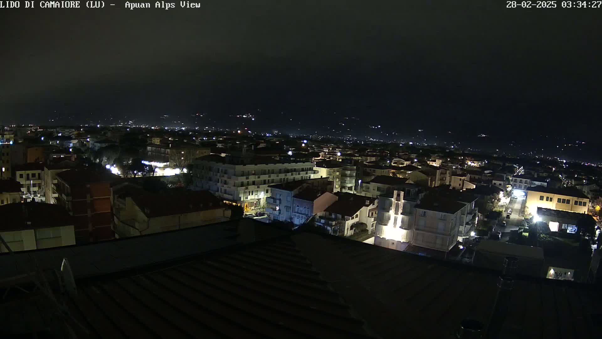 A nighttime aerial view of a town, showing buildings lit up against a dark sky.