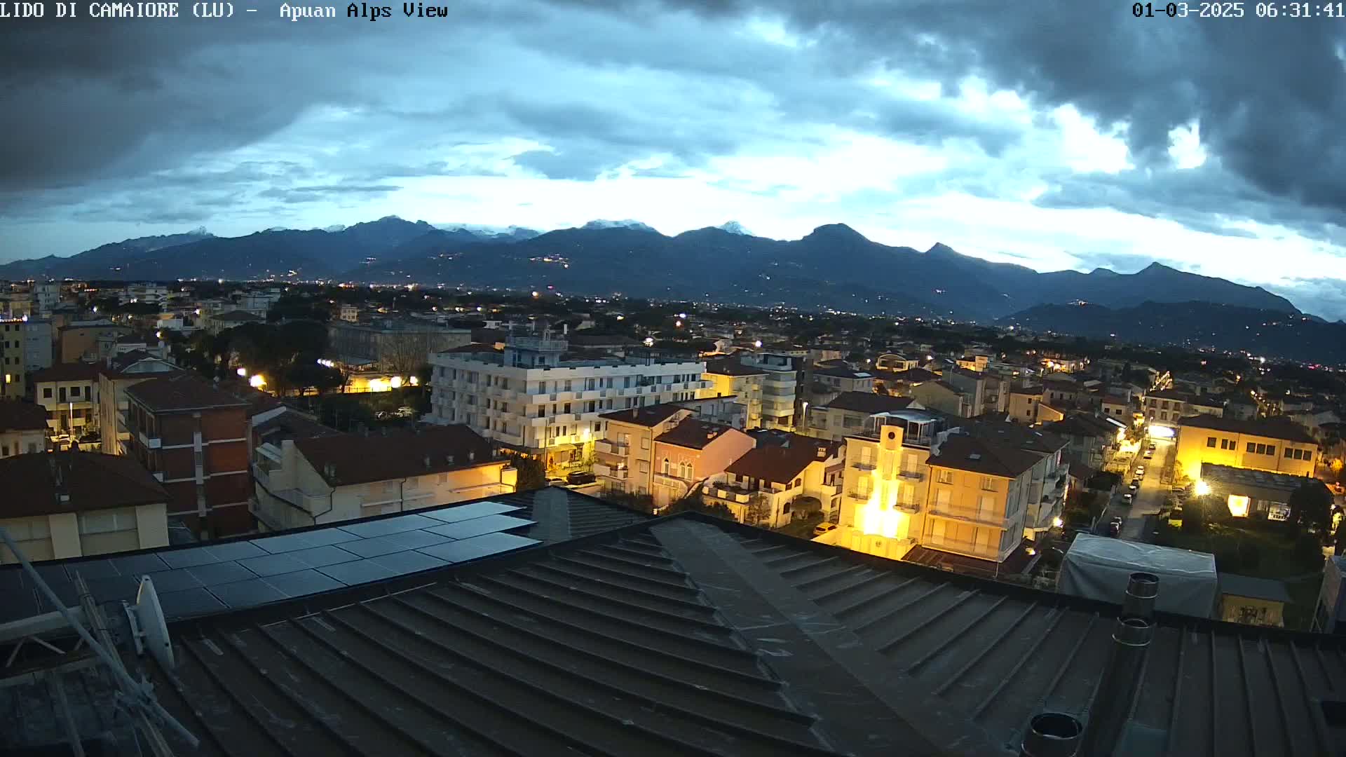 A nighttime view of a town nestled beneath a mountain range under a cloudy sky.