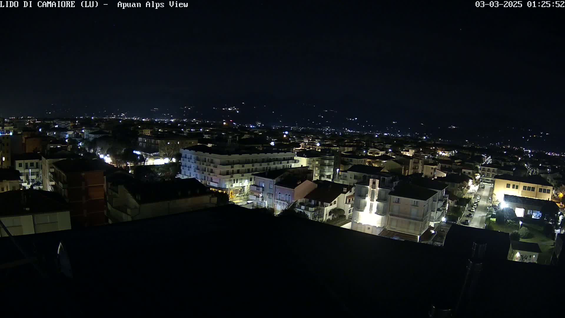 A nighttime aerial view of a town, with the lights of buildings and streets illuminated against a dark sky.