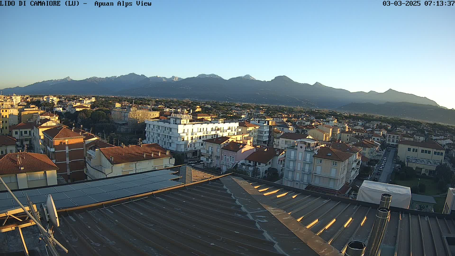 A clear, sunny morning view of a town nestled in a valley, with mountains in the background.