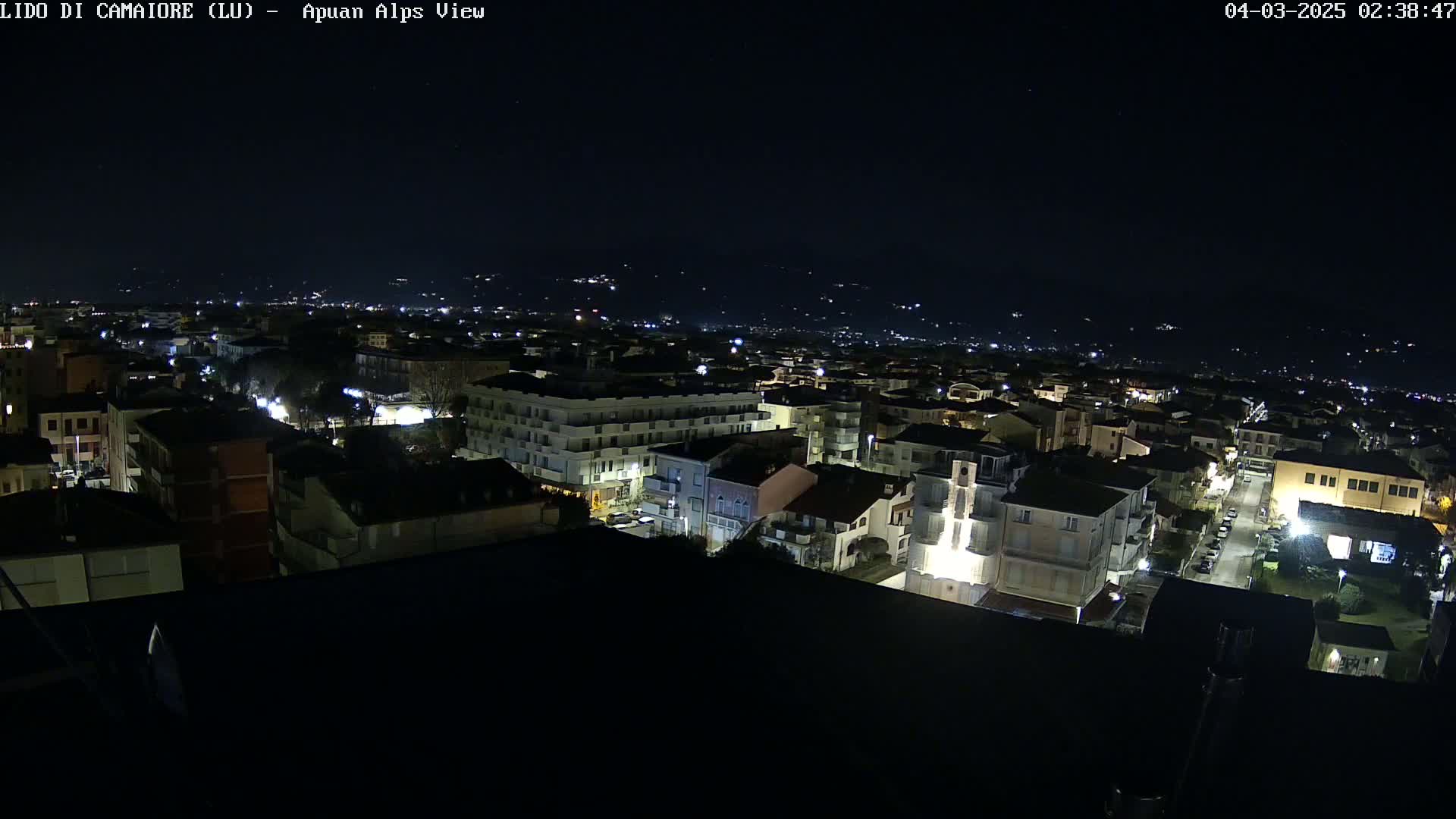 A nighttime aerial view of a town with illuminated buildings and streets, under a clear, dark sky.