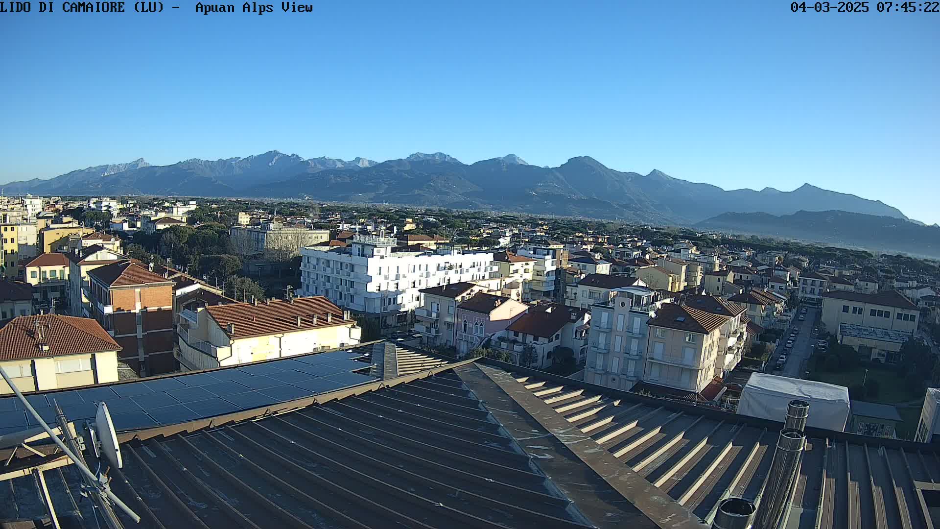 A clear, sunny day reveals a sprawling town nestled against a backdrop of majestic mountains.