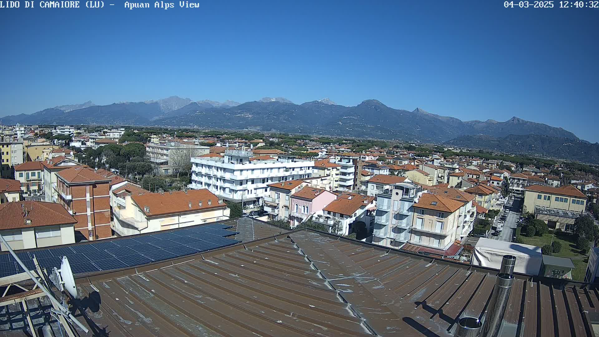 A rooftop view of a town under a clear blue sky, with mountains in the background.