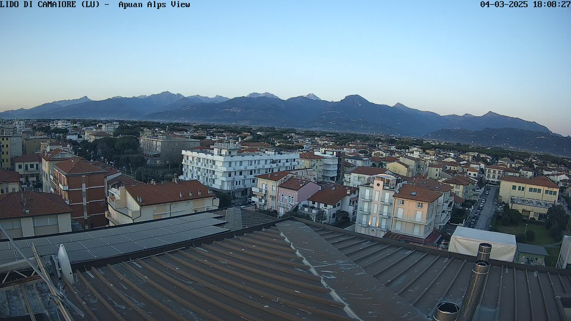 A rooftop view of a town at dusk, overlooking a mountain range under a clear sky.