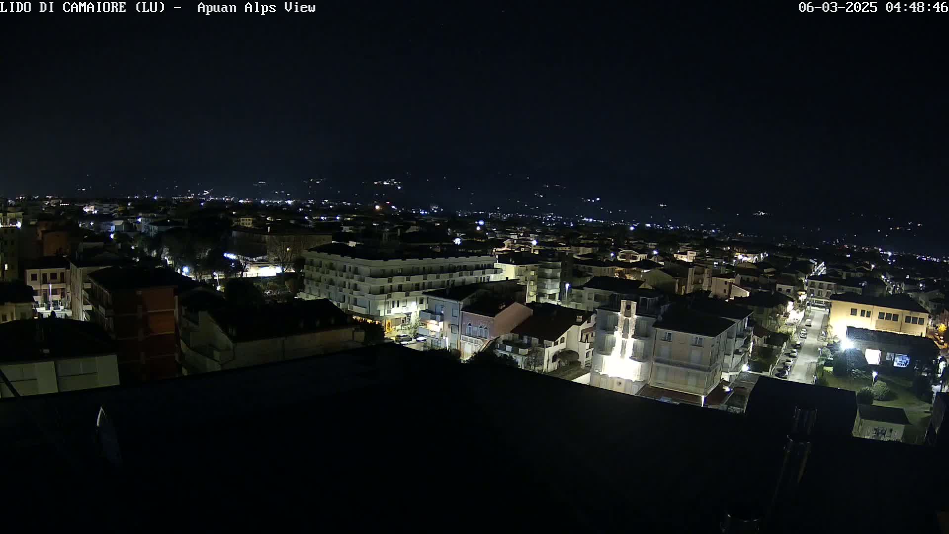 A nighttime, high-angle view of a town with dimly lit buildings and streets, under a dark sky.