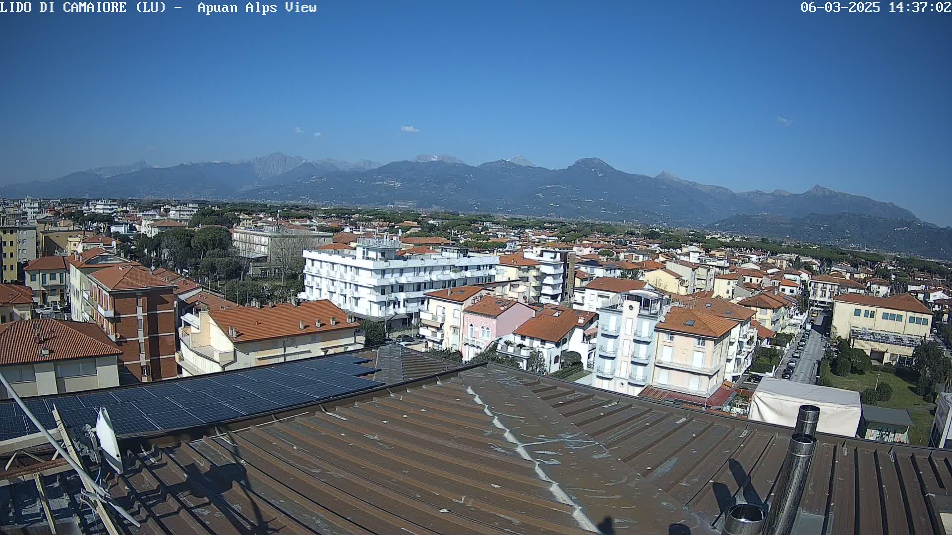 A rooftop view of a town on a clear, sunny day, with a mountain range visible in the distance.