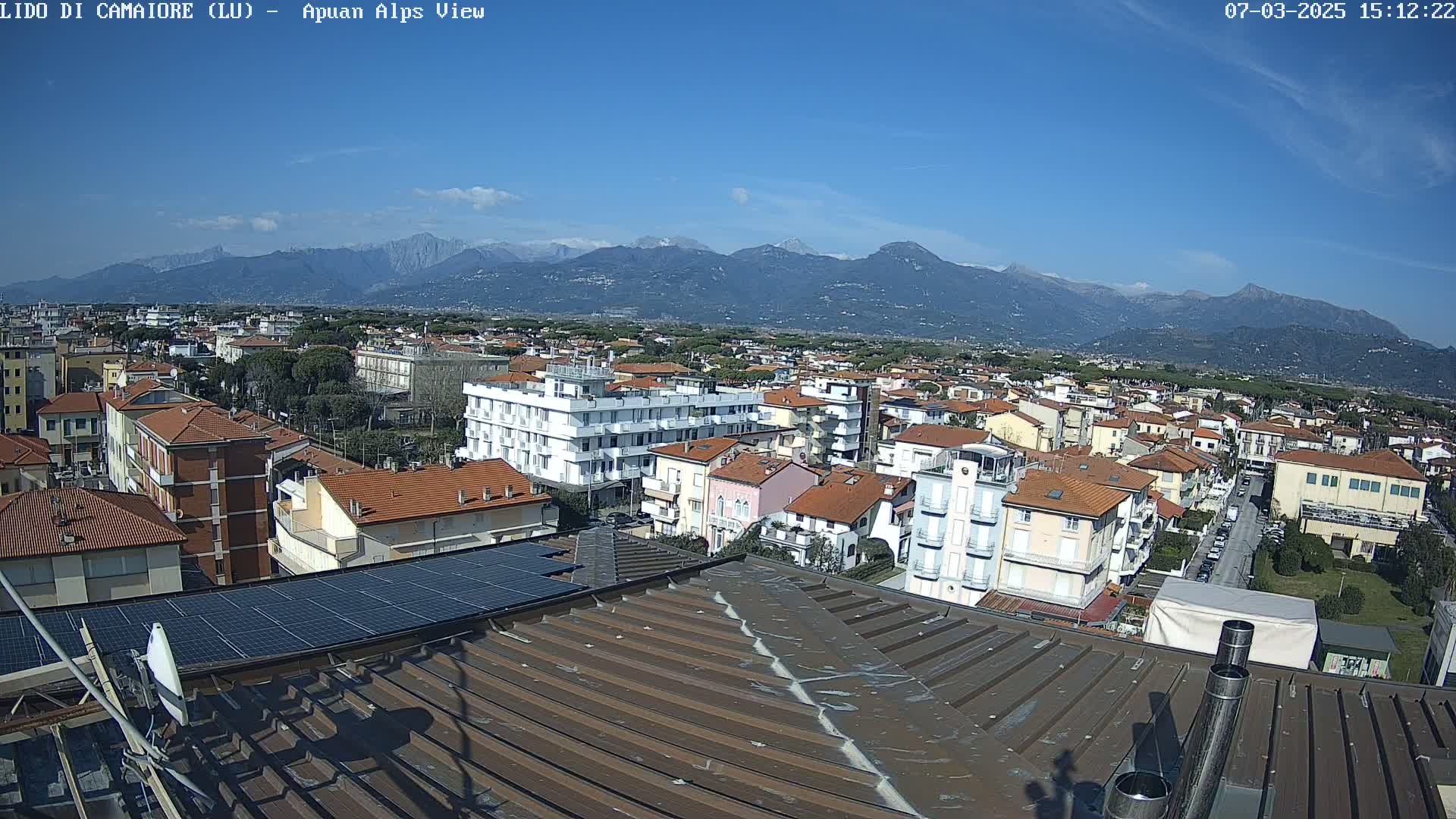 A rooftop view shows a town nestled below a mountain range under a clear blue sky.