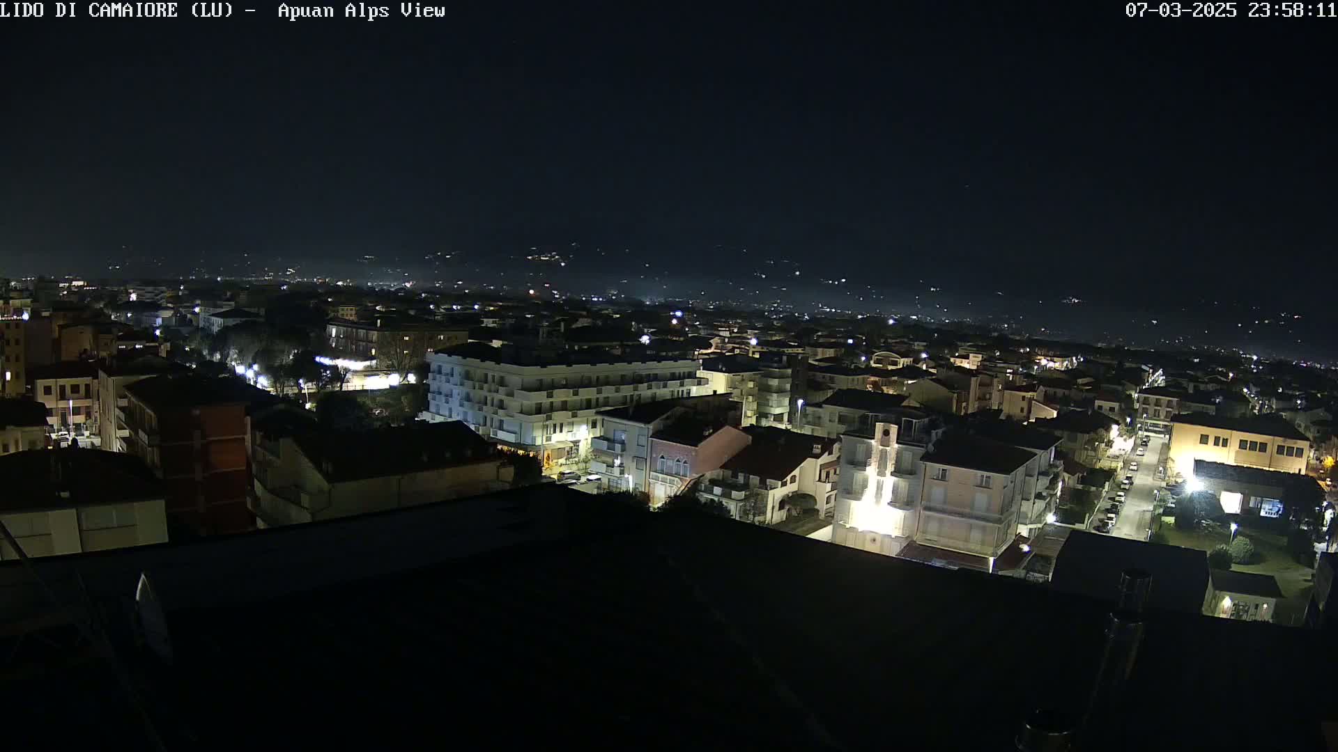 A nighttime aerial view of a town shows a cityscape illuminated by streetlights under a clear, dark sky.
