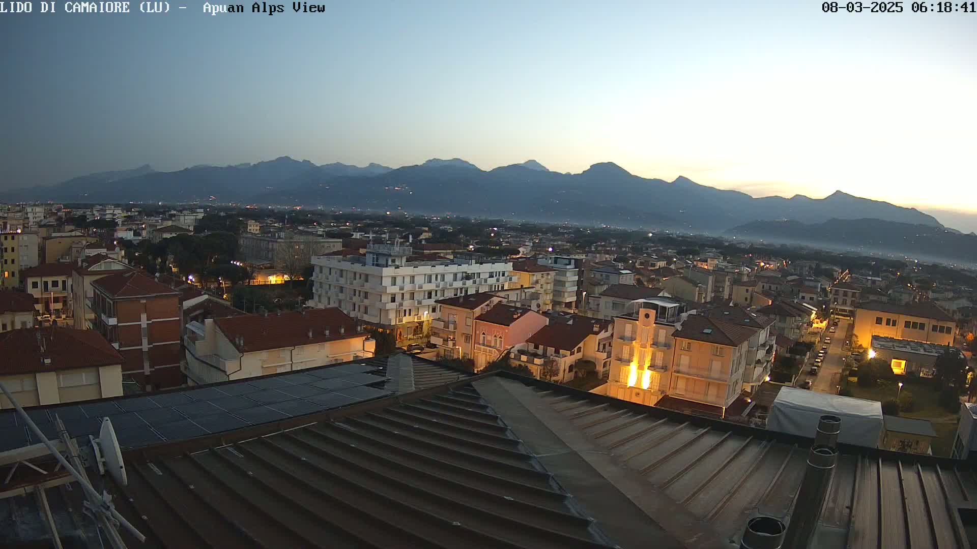 A twilight view of a town nestled at the base of a mountain range under a clear, dusky sky.