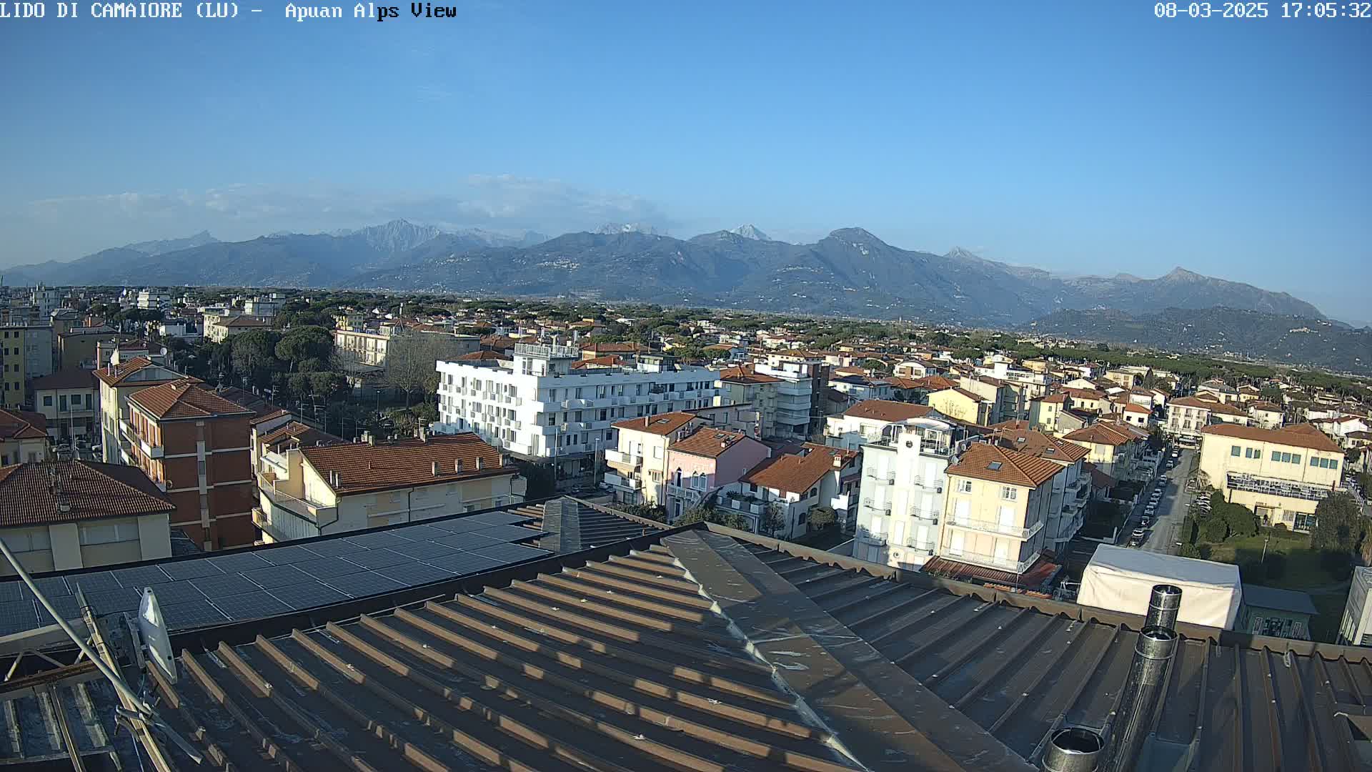 A clear day reveals a view of a town nestled at the foot of distant, snow-capped mountains.