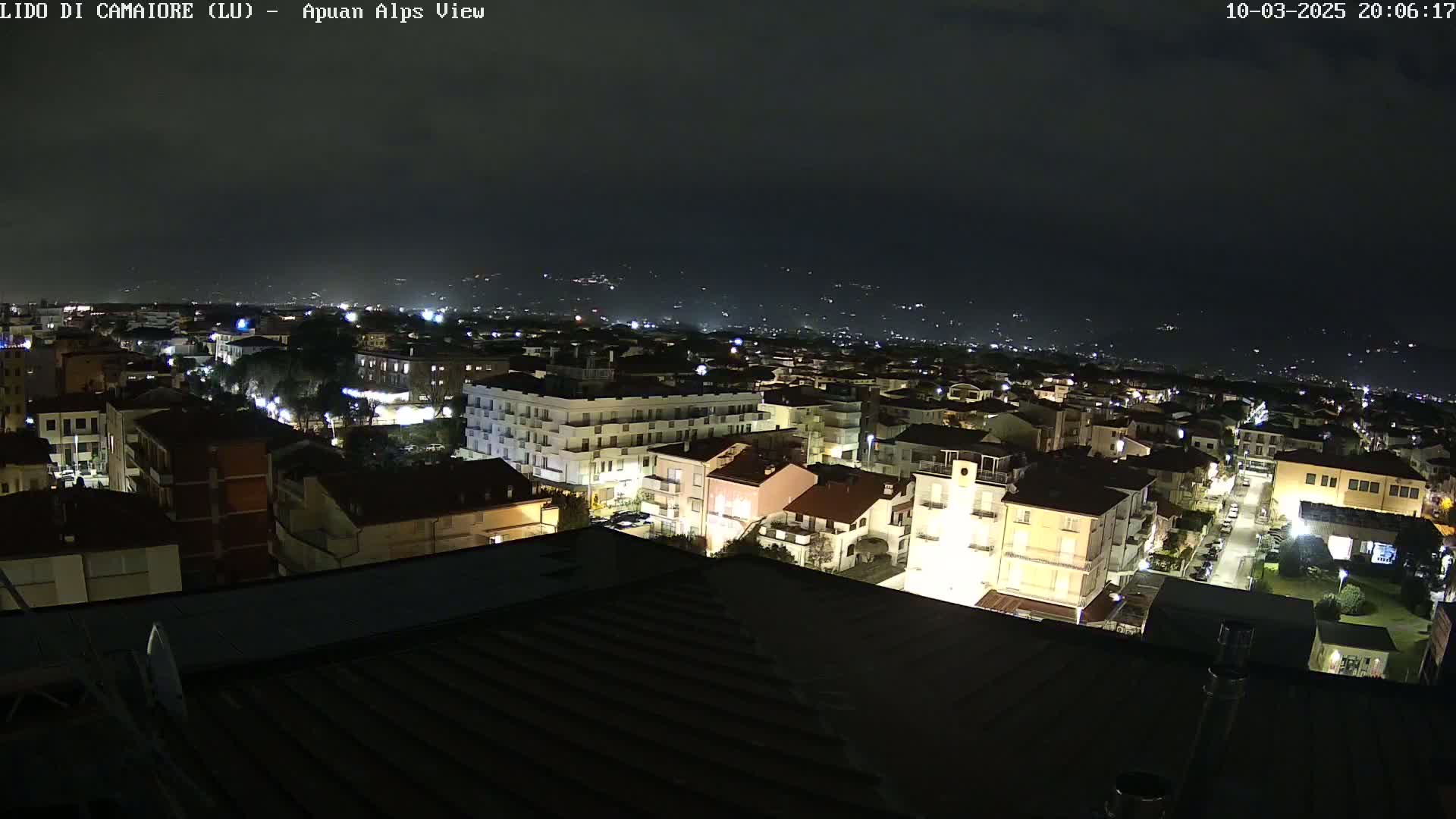 A nighttime view of a town illuminated by streetlights, with distant hills faintly visible under a dark sky.