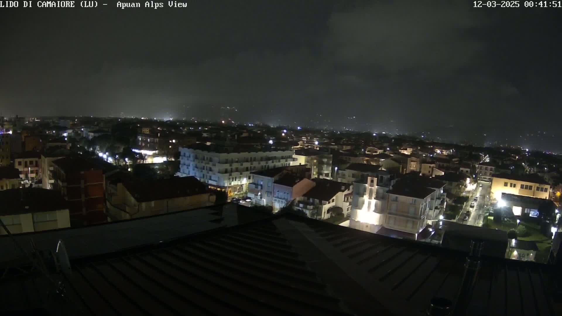 A nighttime view of a town illuminated by streetlights under a dark, cloudy sky.