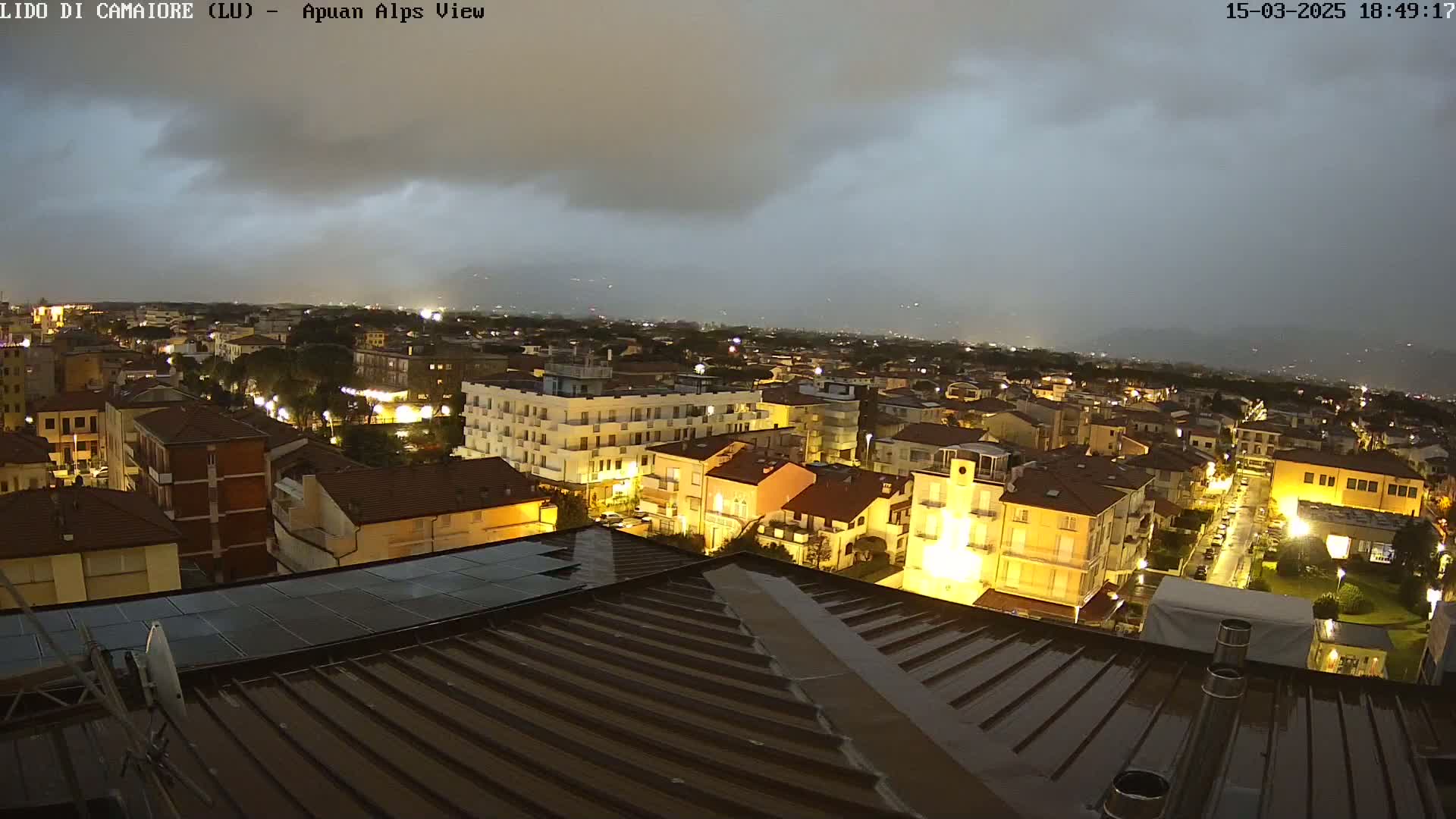 A nighttime view of a town, illuminated by streetlights under a dark, cloudy sky, with rain possibly falling.