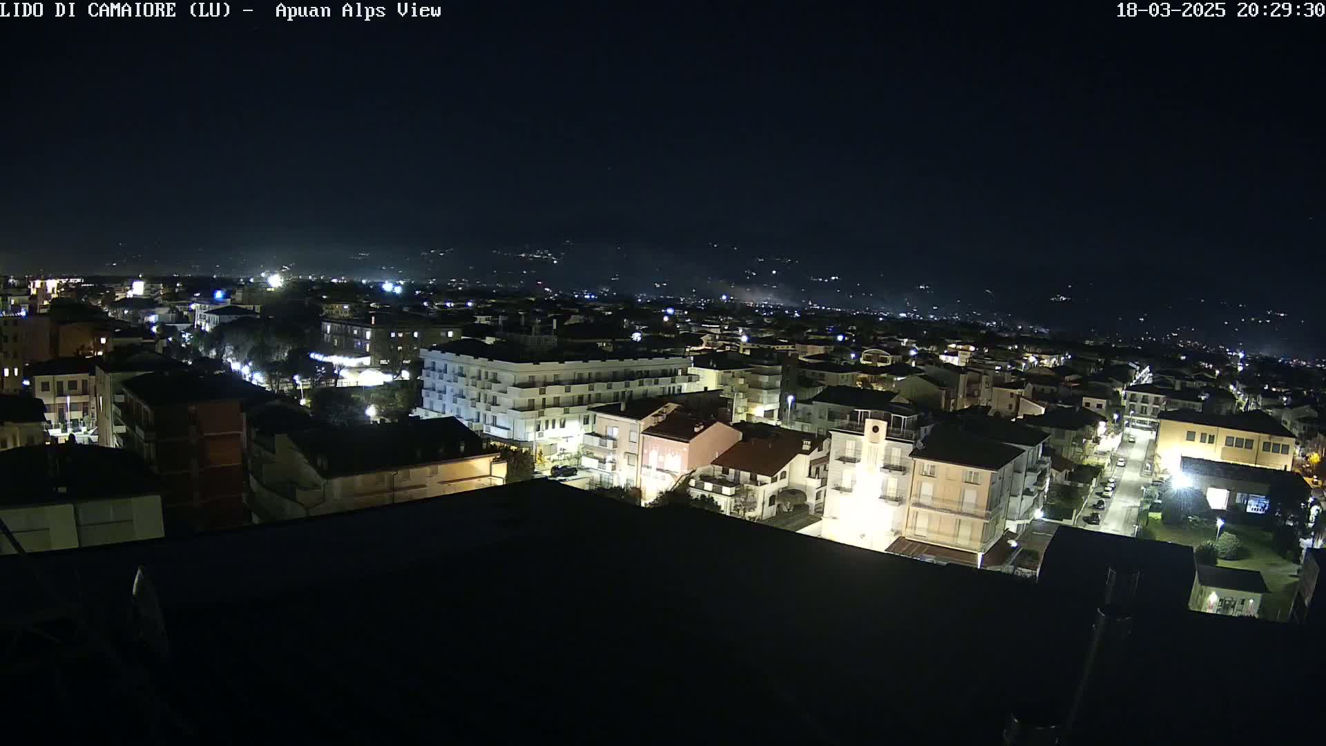 A nighttime aerial view of a town with brightly lit buildings and streets, under a clear, dark sky.
