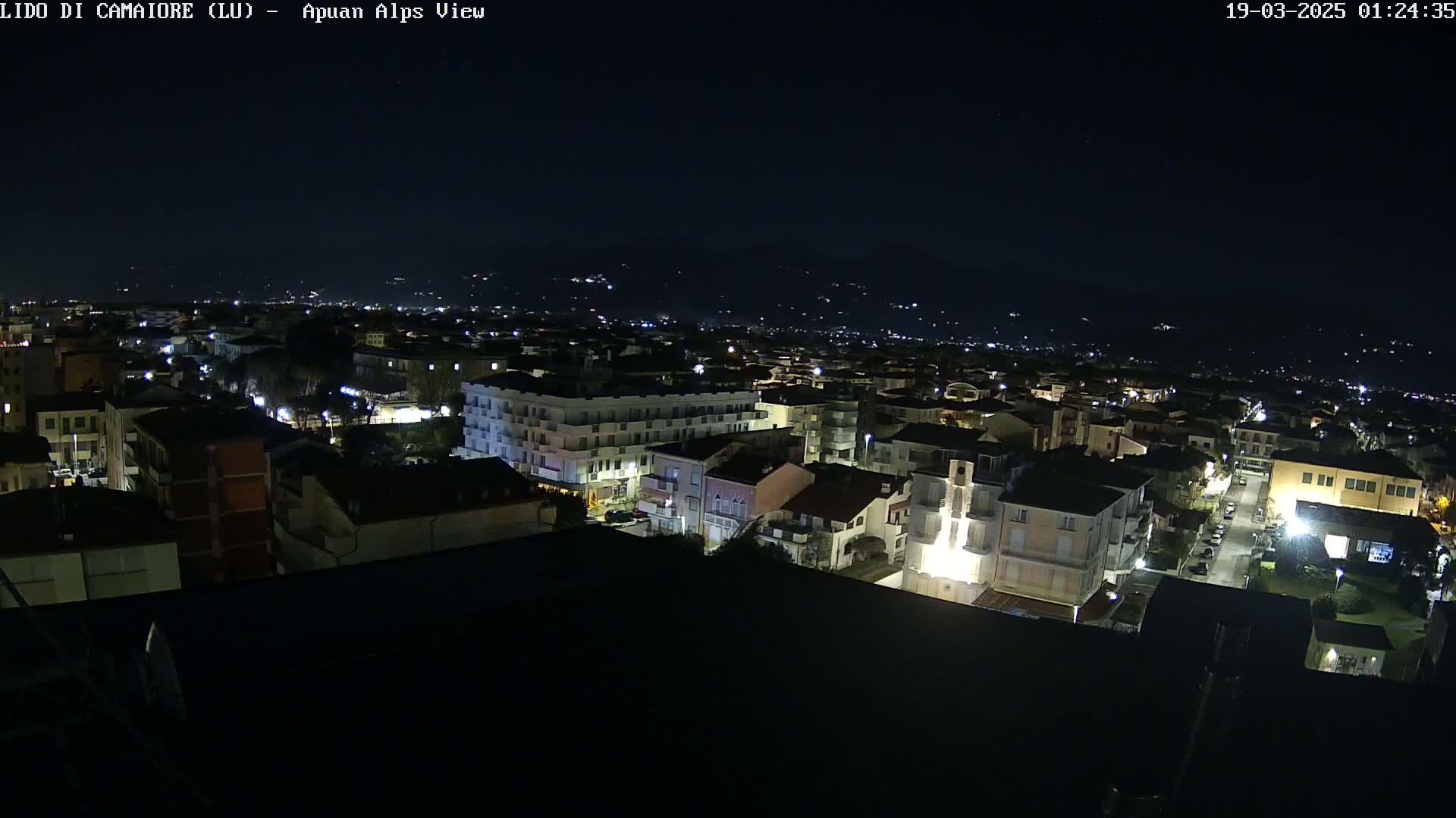 A nighttime, aerial view of a town illuminated by streetlights, with distant mountains visible under a clear, dark sky.
