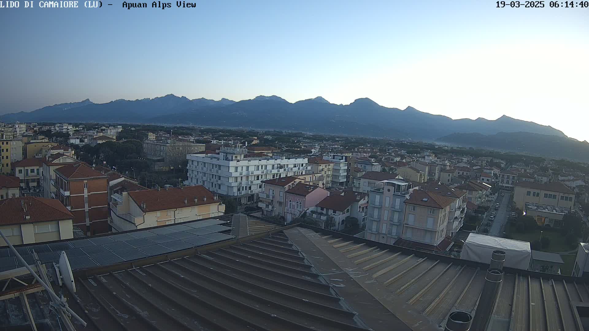 A rooftop view overlooking a town nestled against a mountain range under a clear, twilight sky.